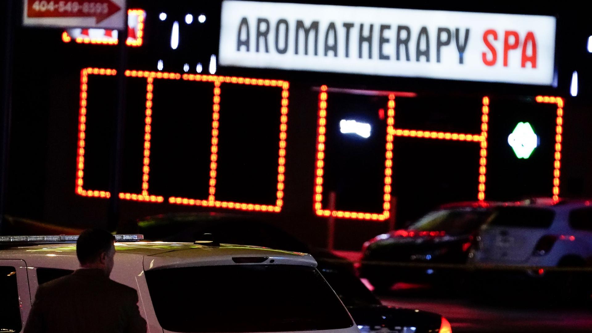 A police SUV is shown in the nearground with a bright white sign in the distance for an Aromatherapy spa.