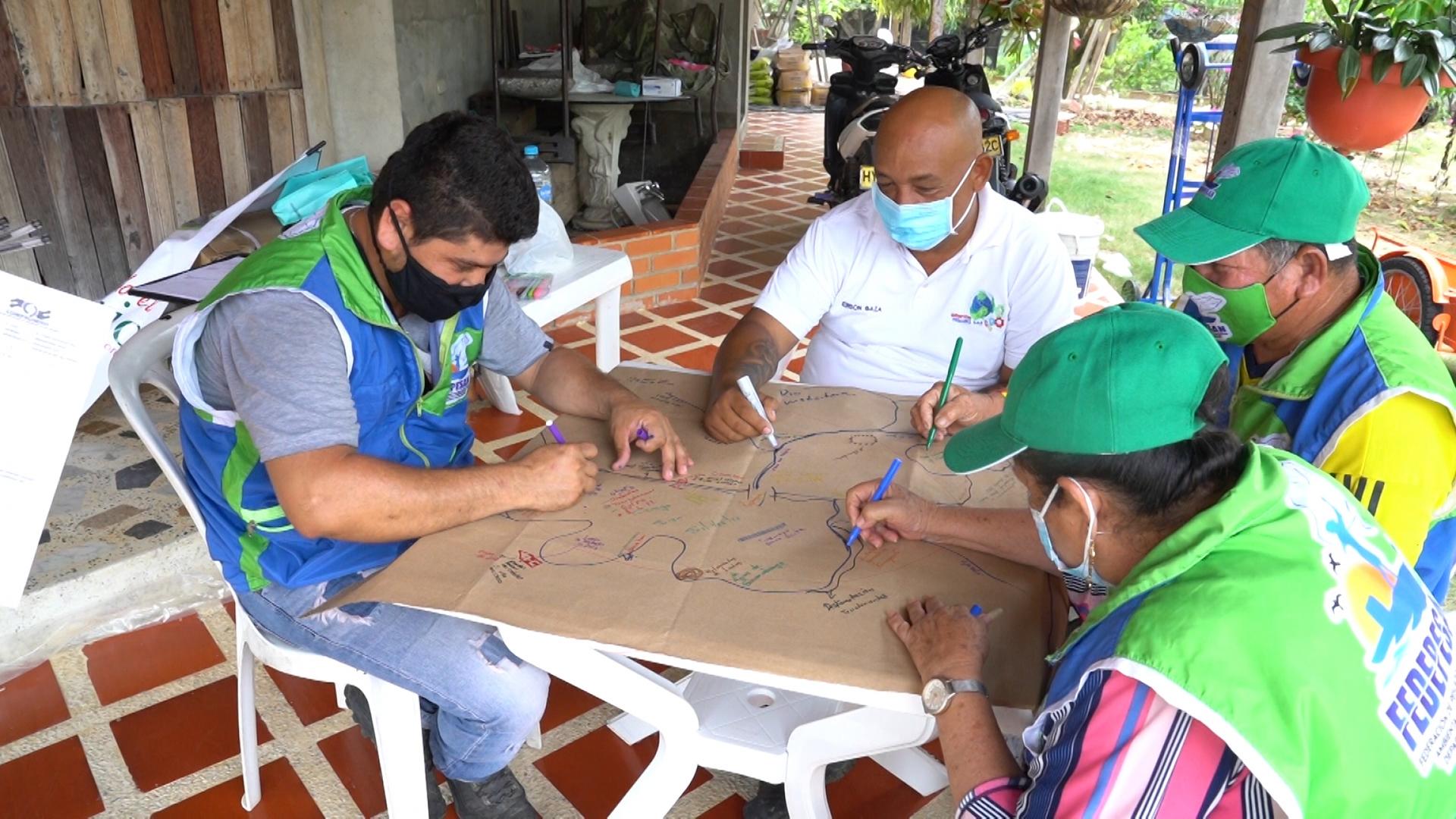A group of people sit around a table and draw a collaborative map of a lake. 