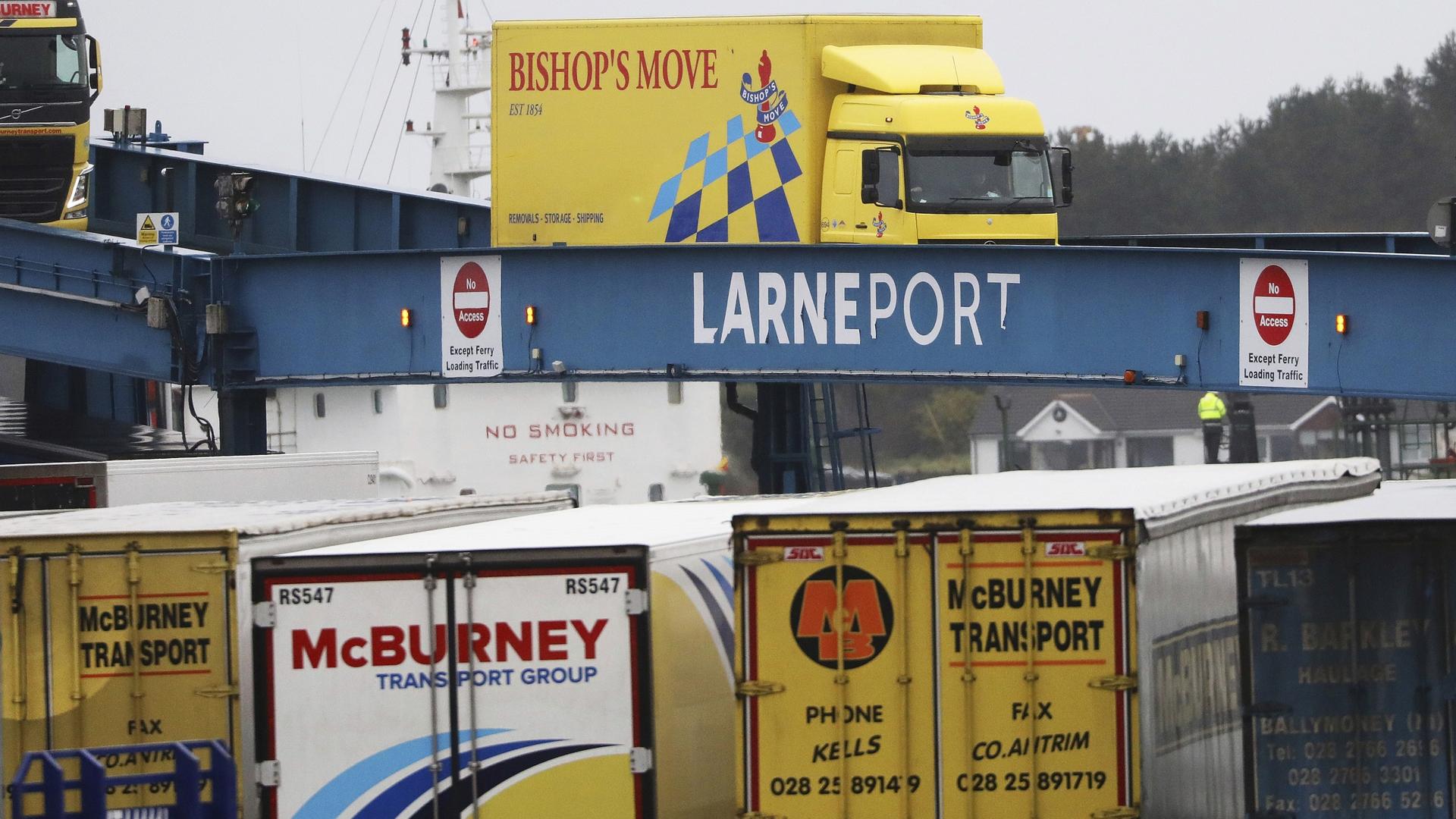 Blue, yellow, and white vehicles disembark from a ferry arriving from Scotland.  