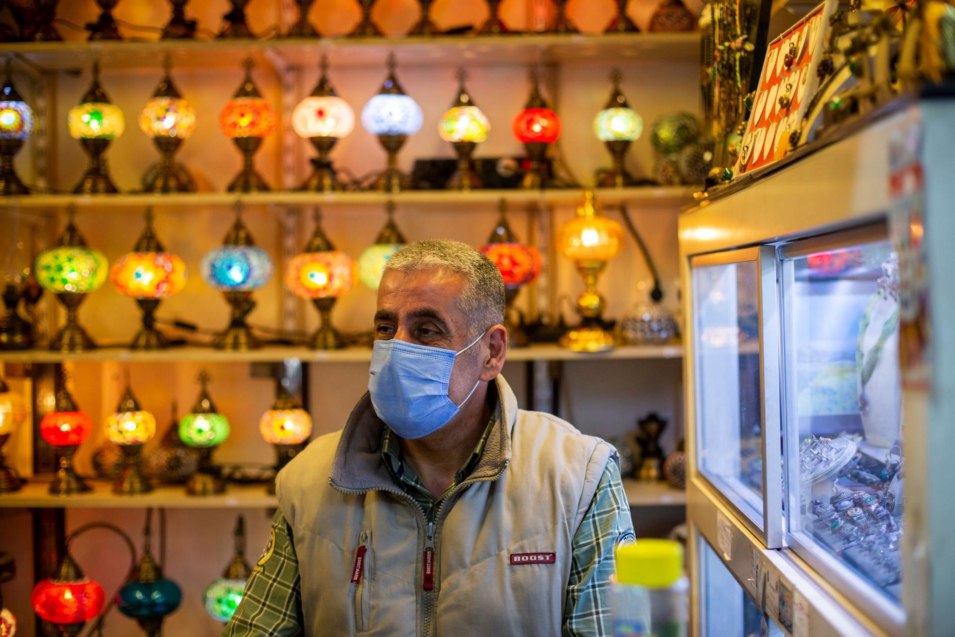 A man is shown with a face mask and standing in front of a wall of brightly colored lamps.