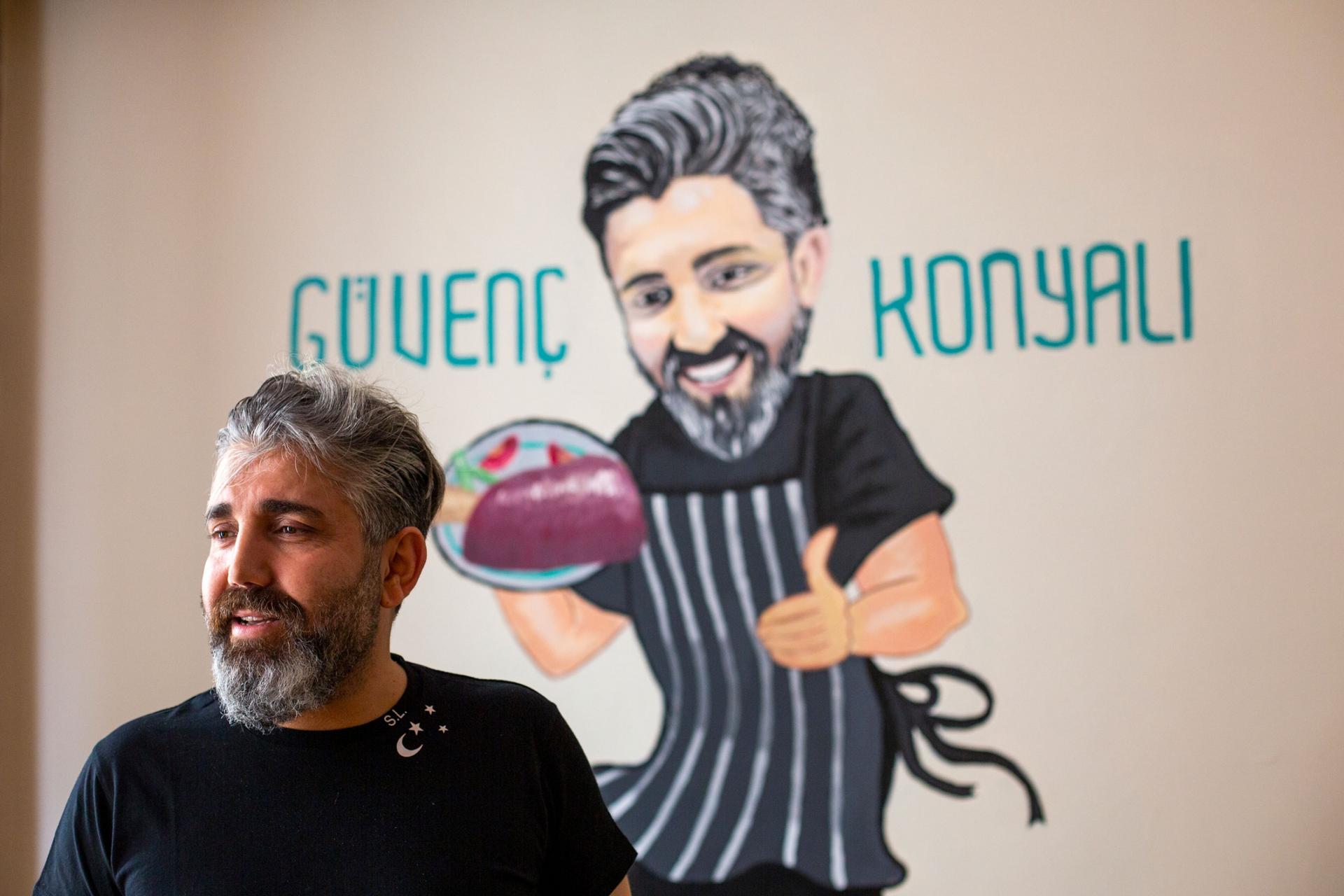 A man is shown with a salt and pepper beard and wearing a black shirt with an illustration of a chef behind him.