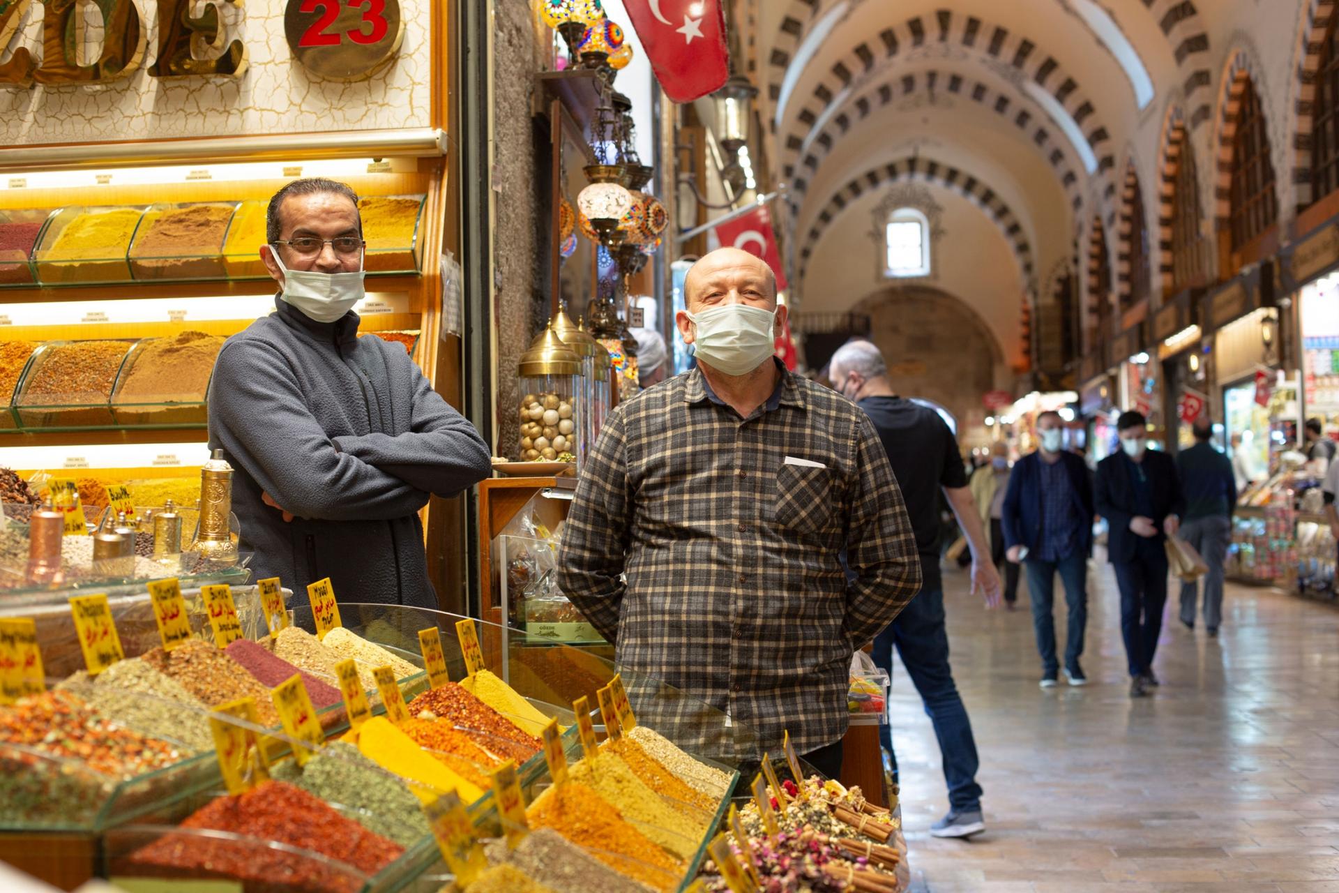 Two men are shown wearing face masks and standing next to a large display of sweets.