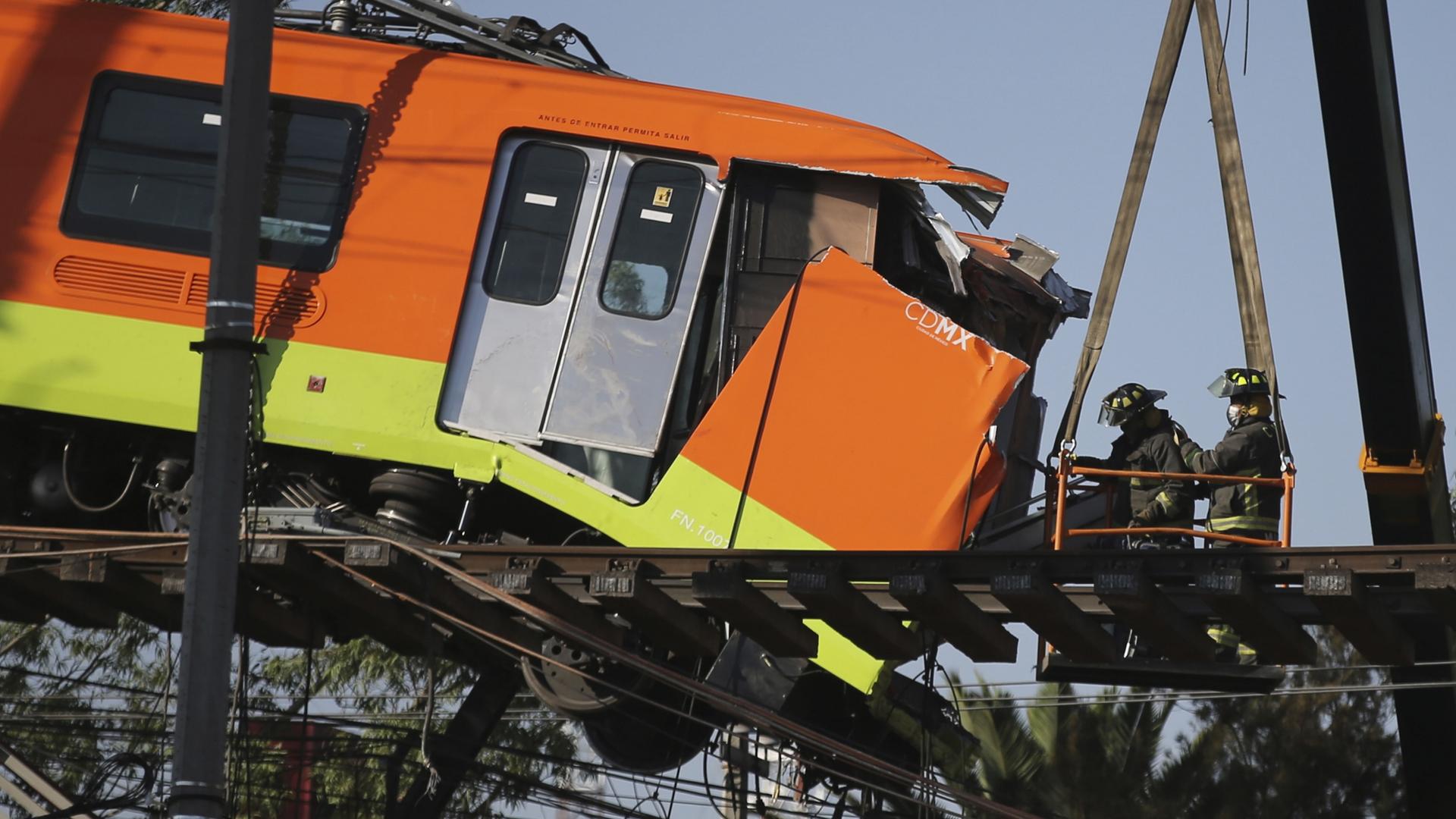 Firefighters work to lower to the ground a subway car dangling from a collapsed elevated section of the metro, in Mexico City, Tuesday, May 4, 2021. 