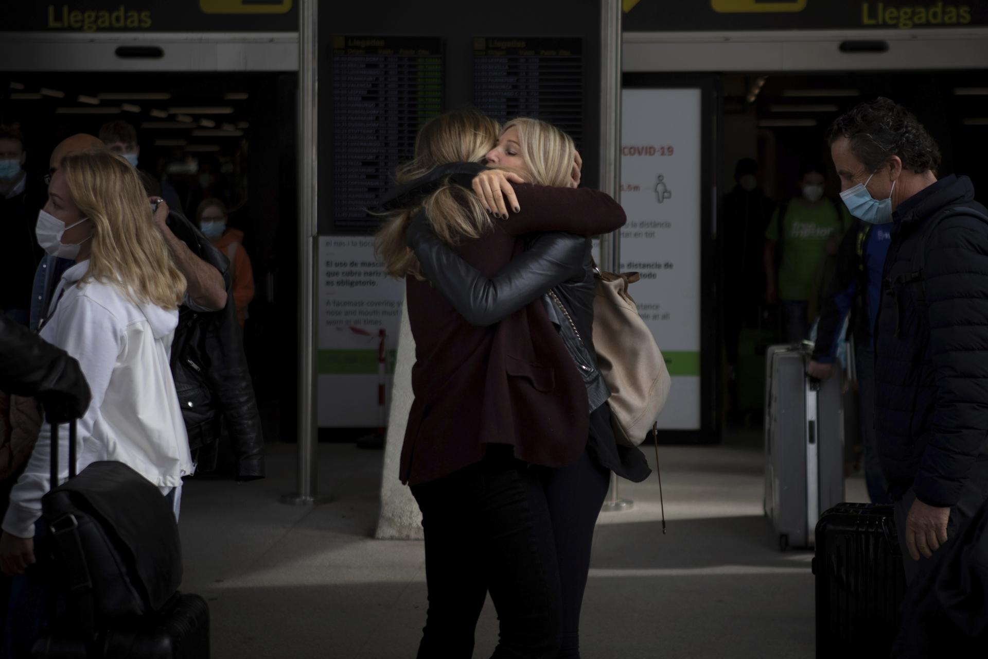 Two women in black clothing embrace in an airport