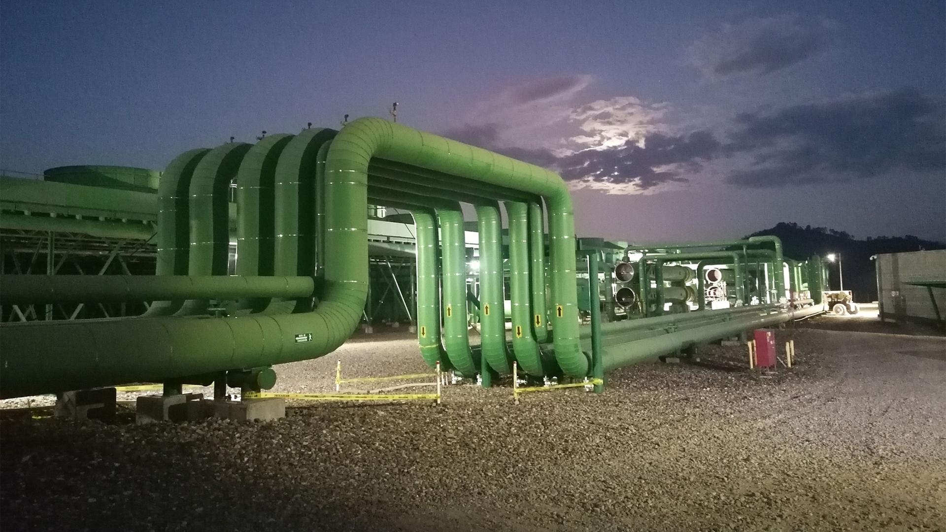Huge green pipes on sandy ground against a dark blue sky