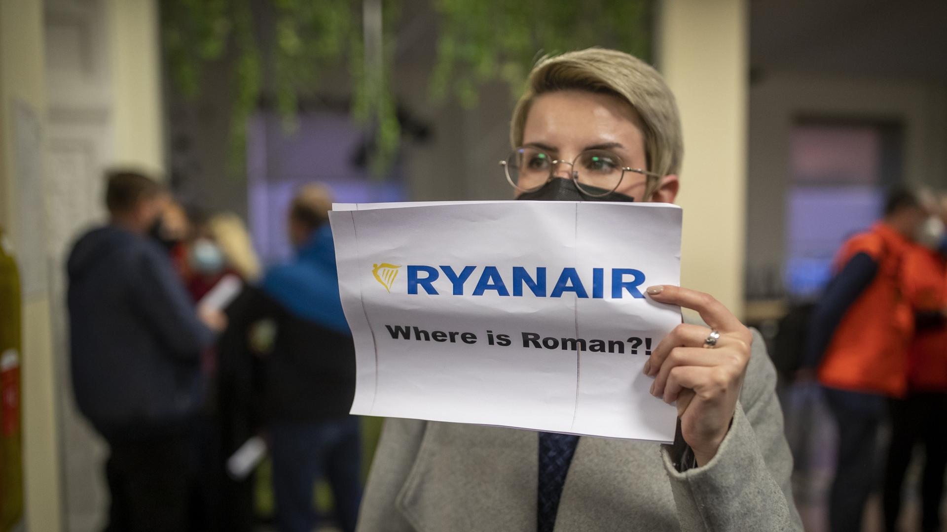 A woman holds a poster reads, "Where is Roman?" as she waits to see passengers de-board Ryanair 
