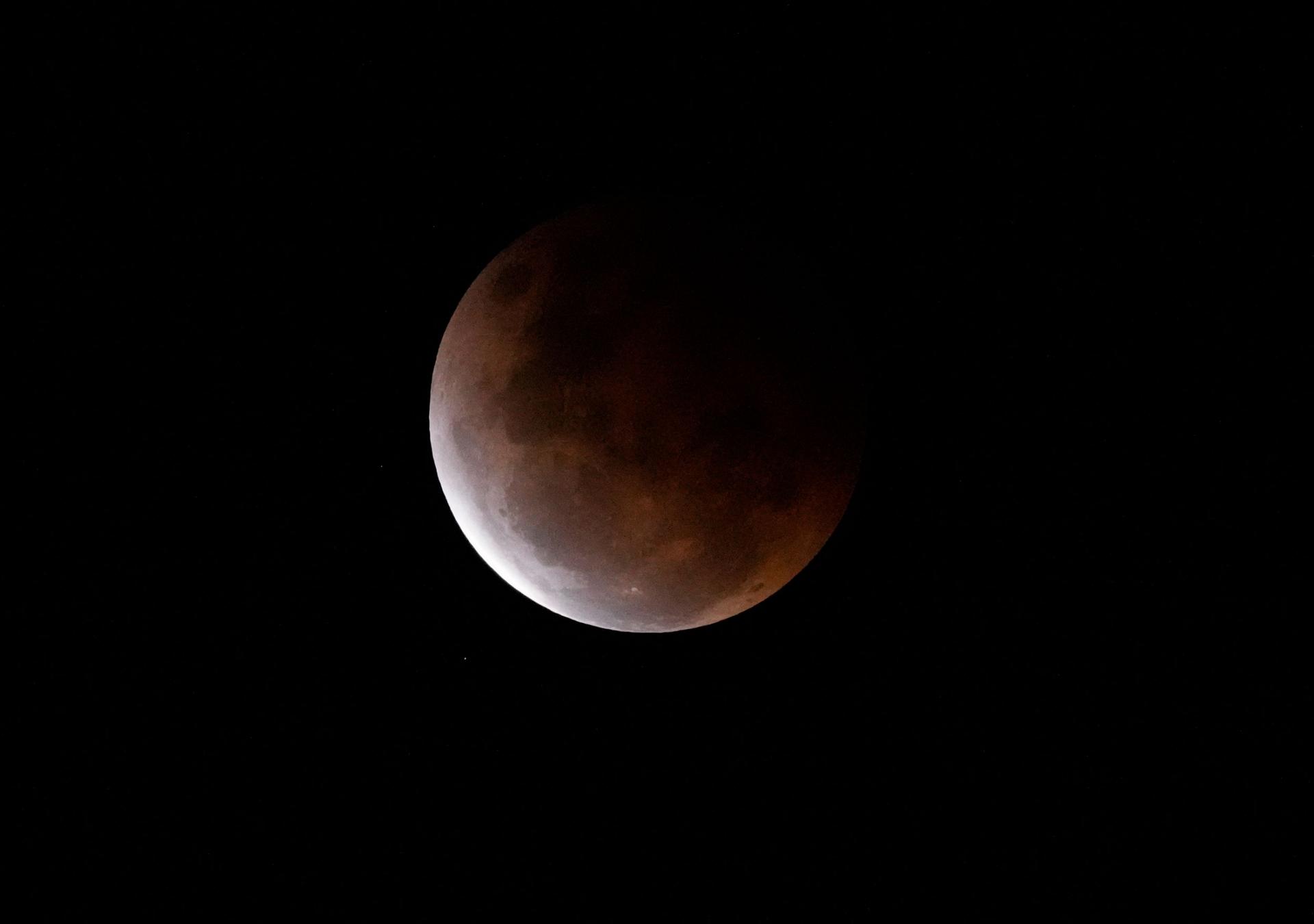 The super blood moon shown with the sun's orange colors reflected on the surface.
