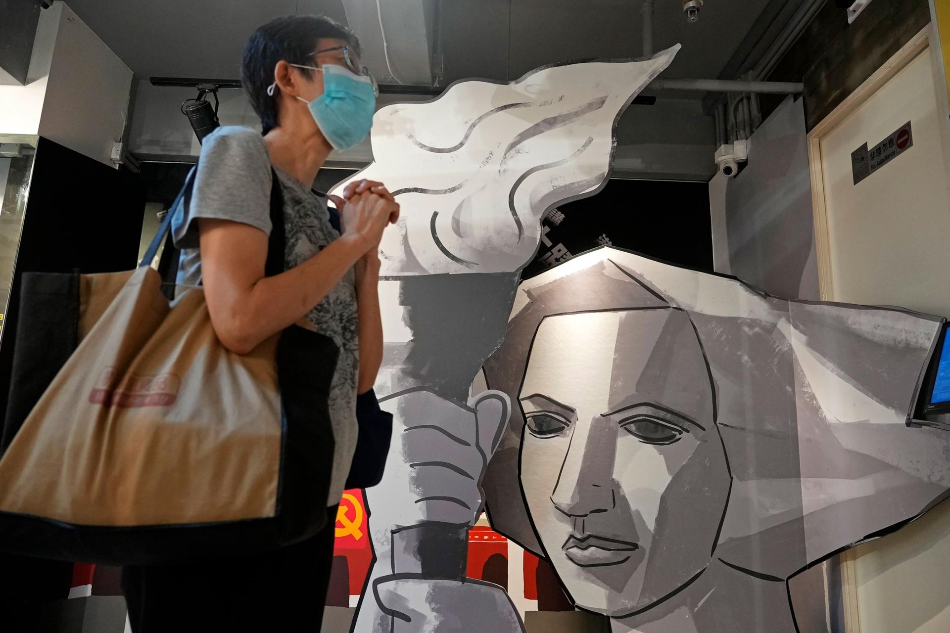 A person is shown with a bag over their shoulder and standing next to an silver artwork of a woman holding a torch with flame.