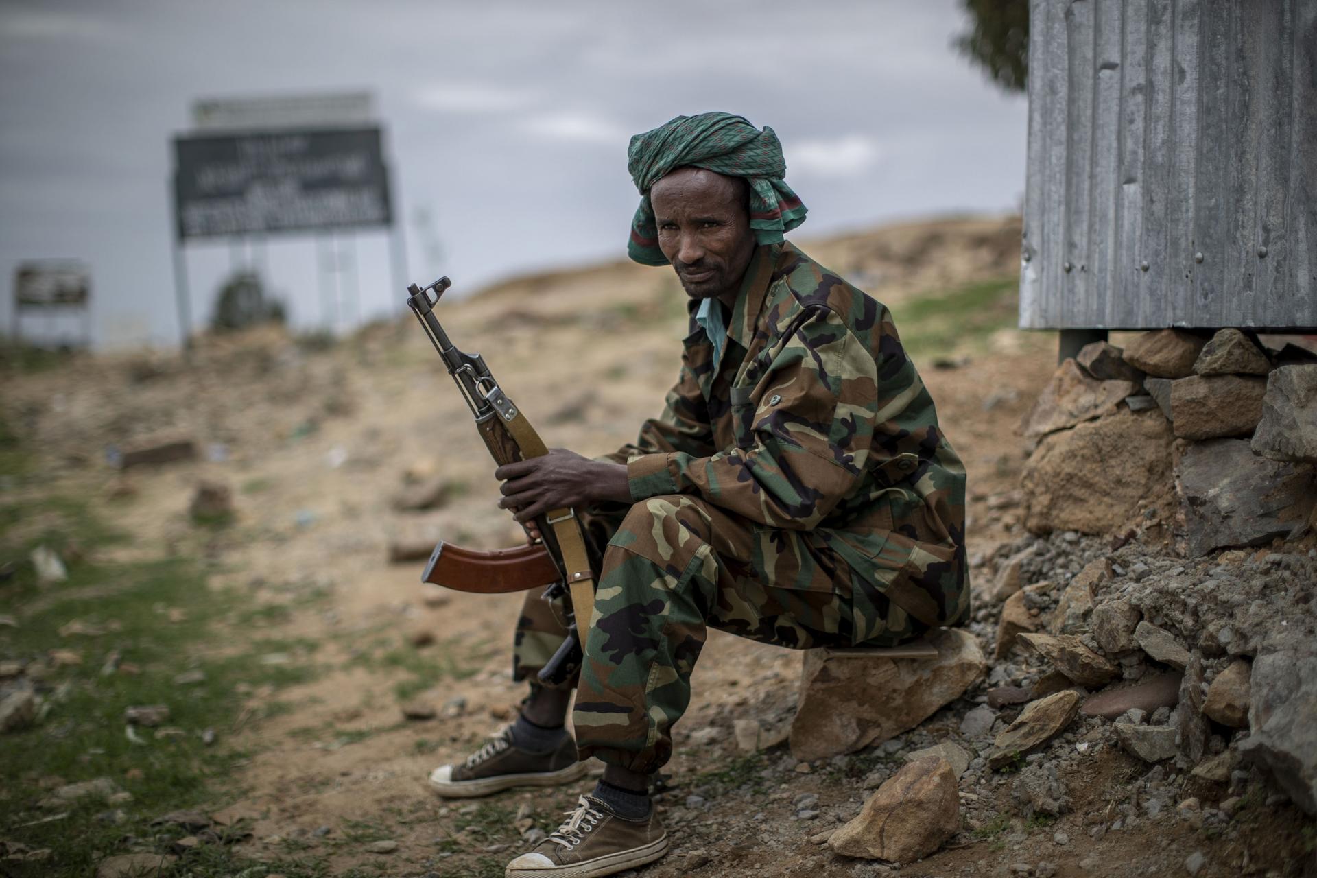 A soldier holds his gun while sitting done. 