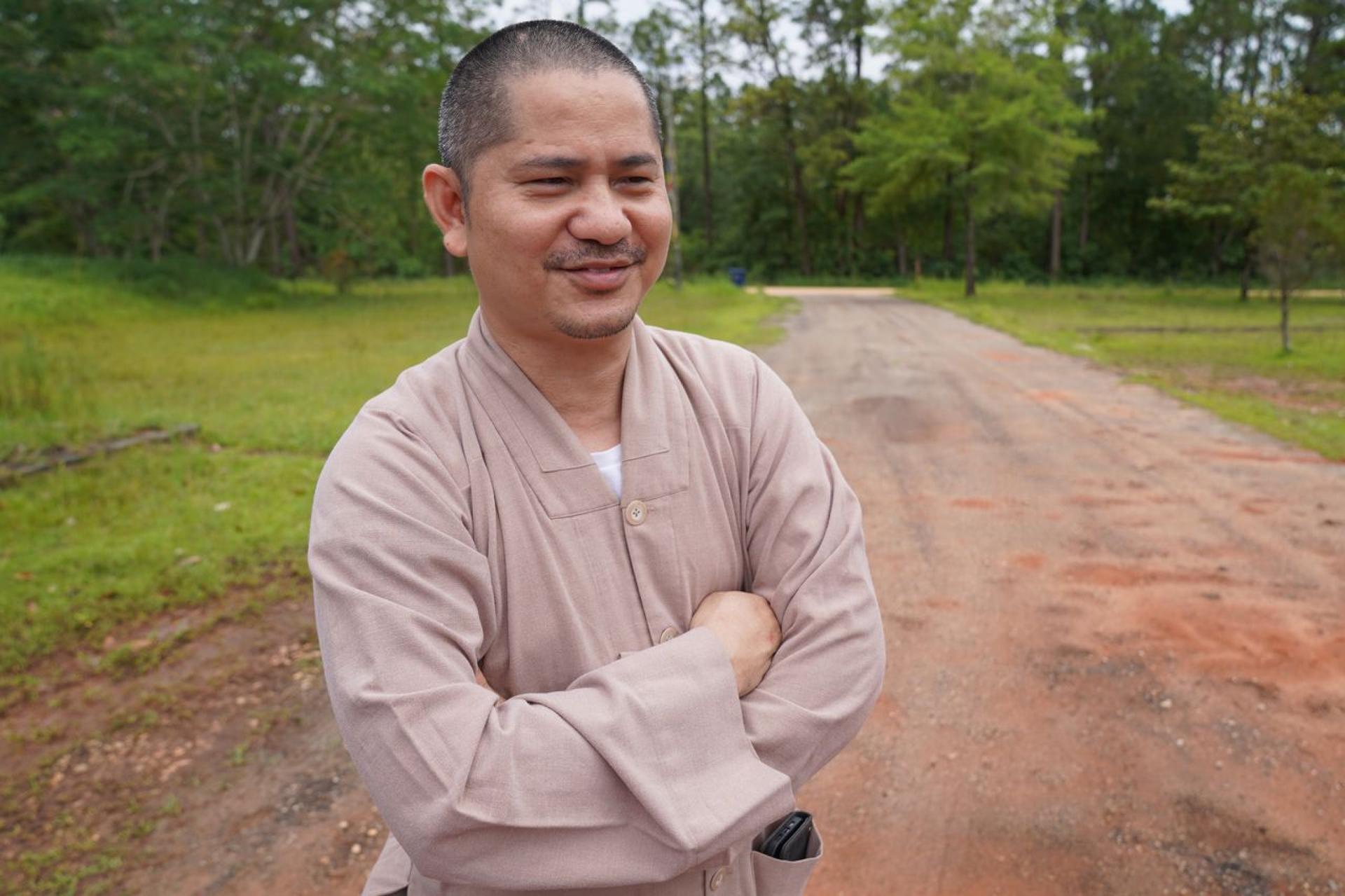 A man smiles while standing with his arms folded