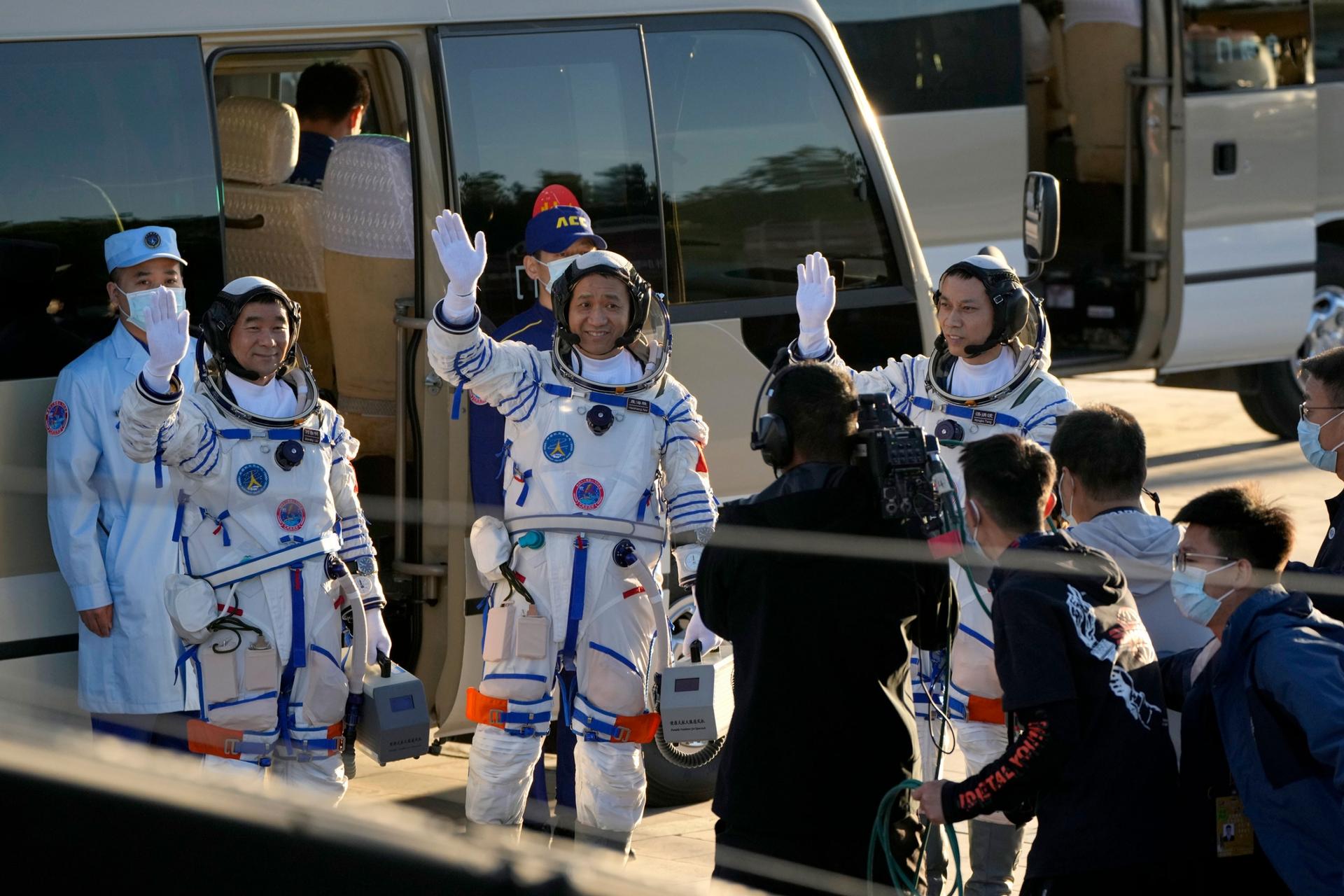 Chinese astronauts are shown wearing white and blue stripped space suits and waiving.