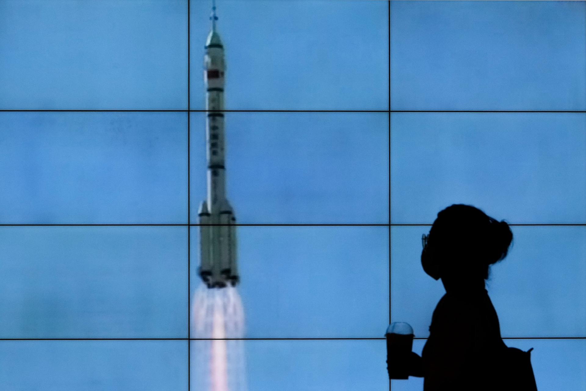 A woman is shown in shadow standing in front of a screen showing the Chinese spacehip lifting off.
