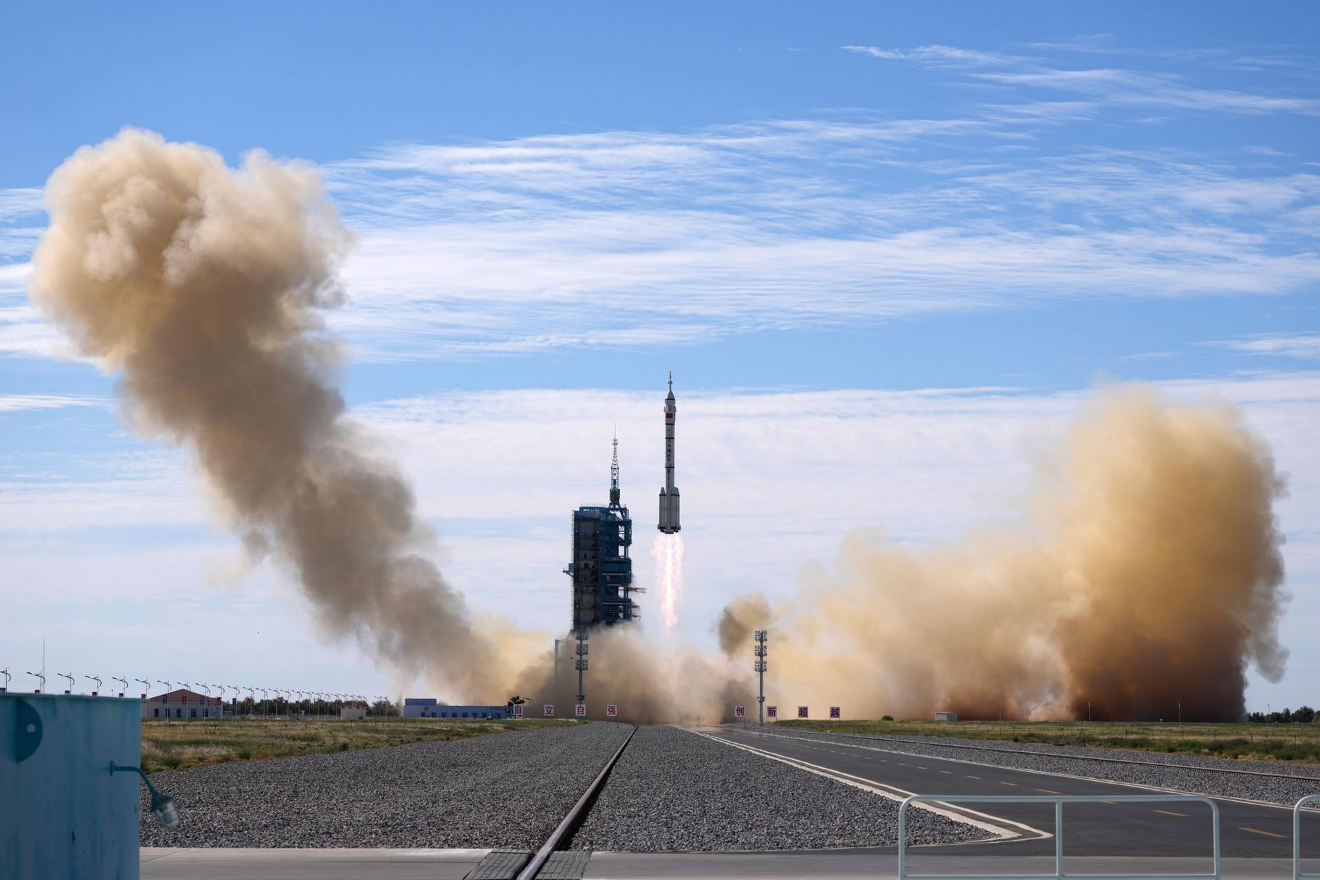 A spaceship is shown in the far distance being lifted into the sky via rockets with smoke billowing.