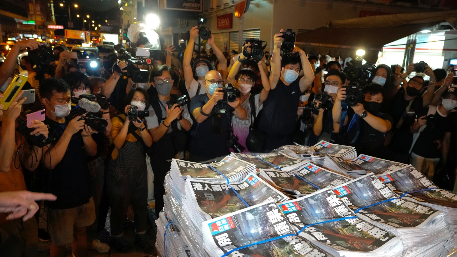 Several stacks of the last edition of the Apple Daily newspaper are shown a group of photographers in the background.