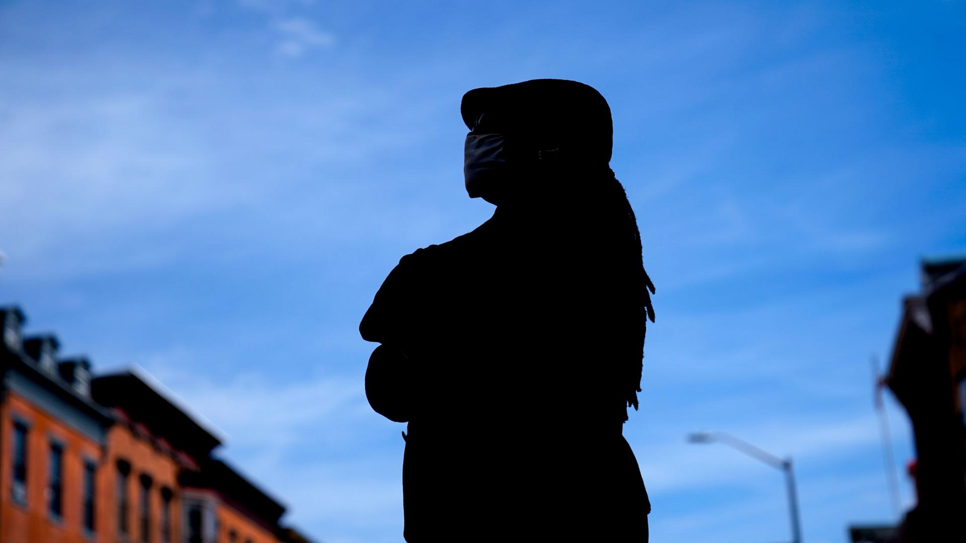 A woman stands in silhouette against a blue sky. 