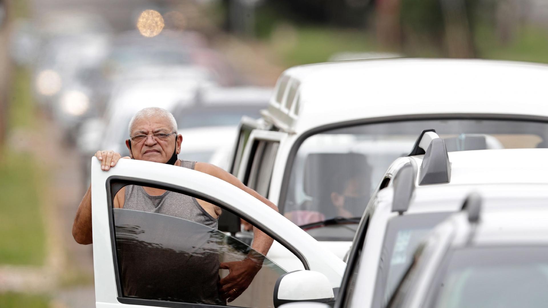 In this March 22, 2021 file photo, a man stands next to his vehicle in a line at a COVID-19 vaccination point for priority elderly persons in the Ceilandia neighborhood, on the outskirts of Brasilia, Brazil. 