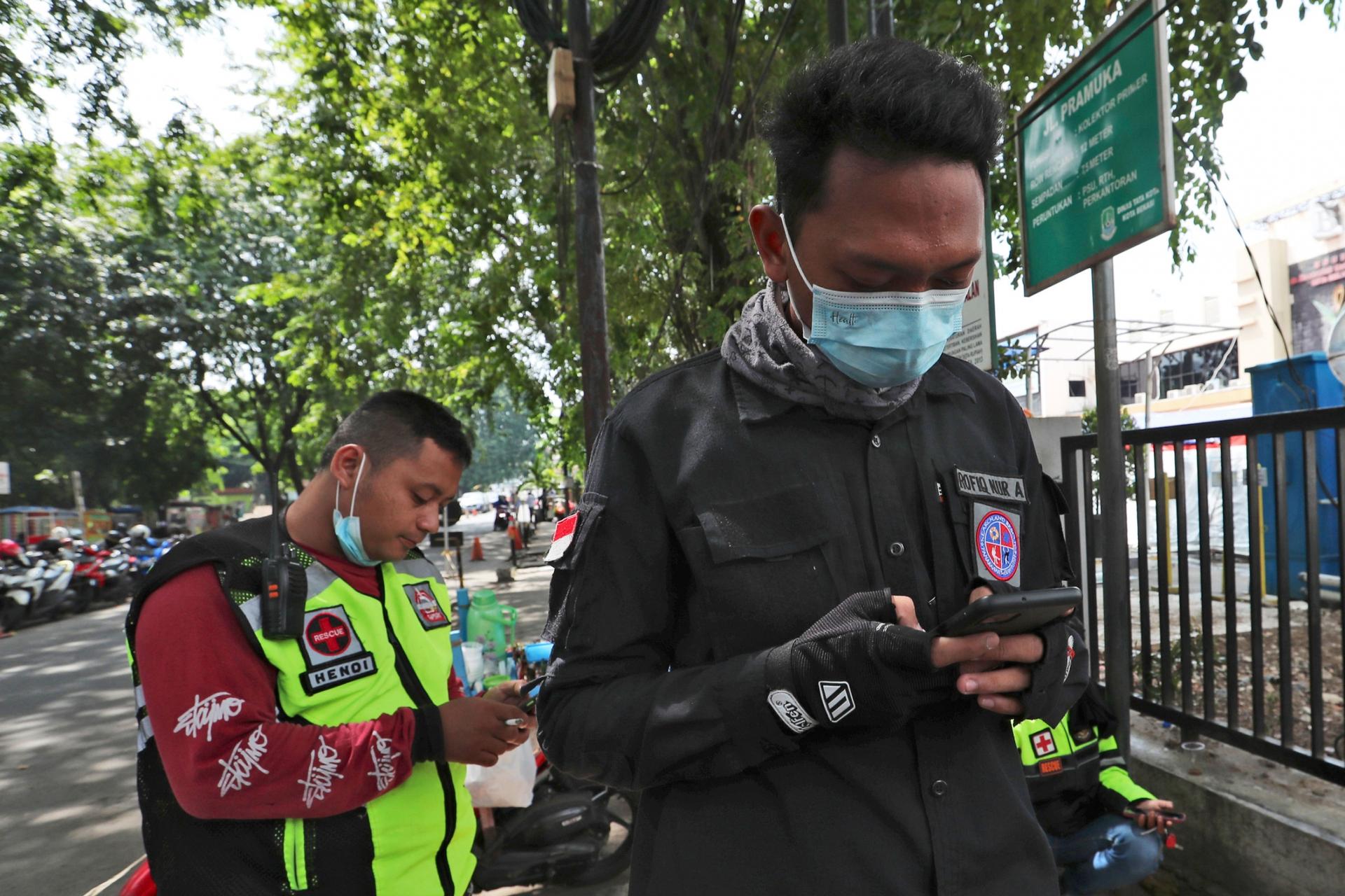 Two men are shown looking down at their mobile phones while wearing medical face masks.