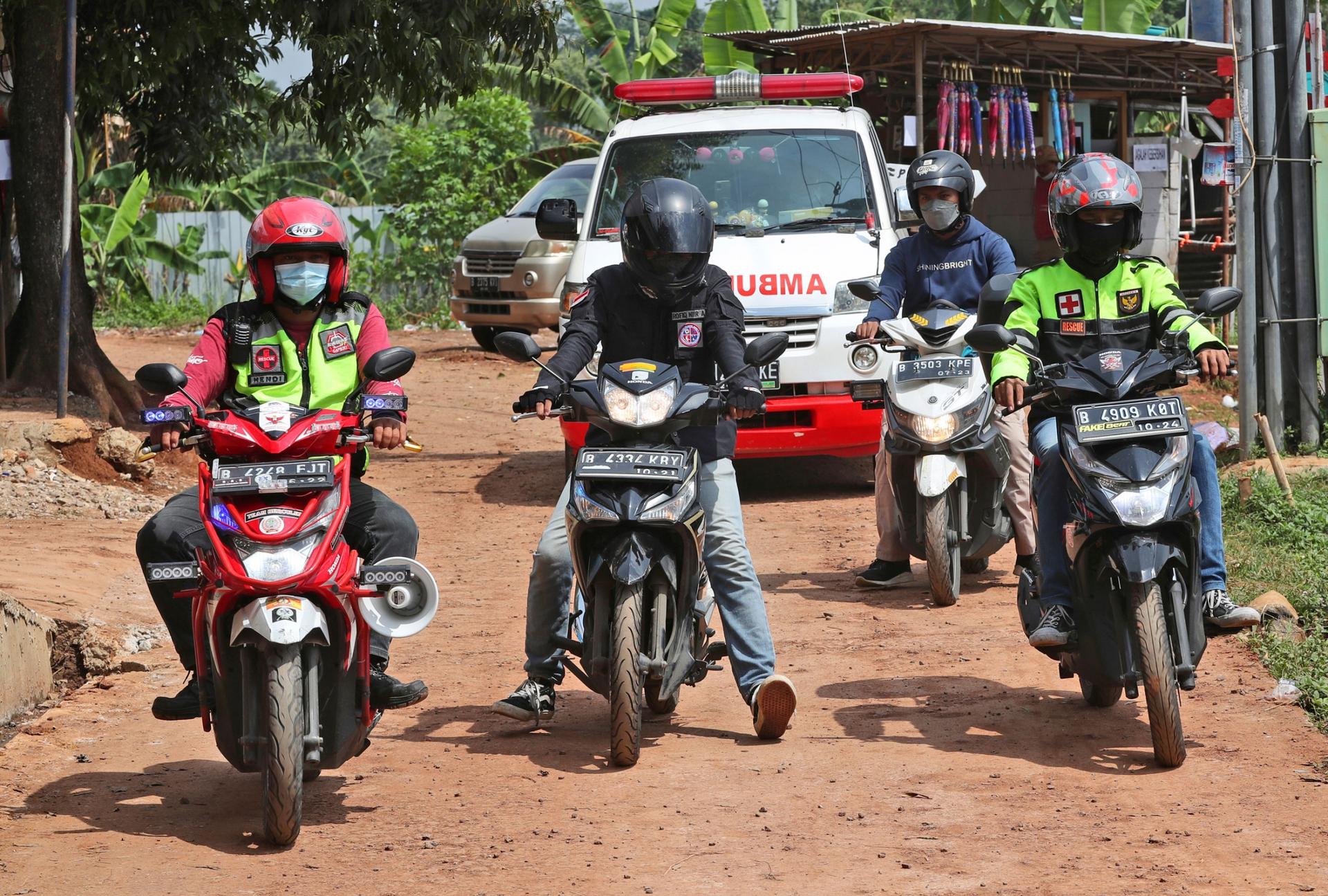 Four people on motorbikes are shown wearing helmets with an ambulance driving behind them.