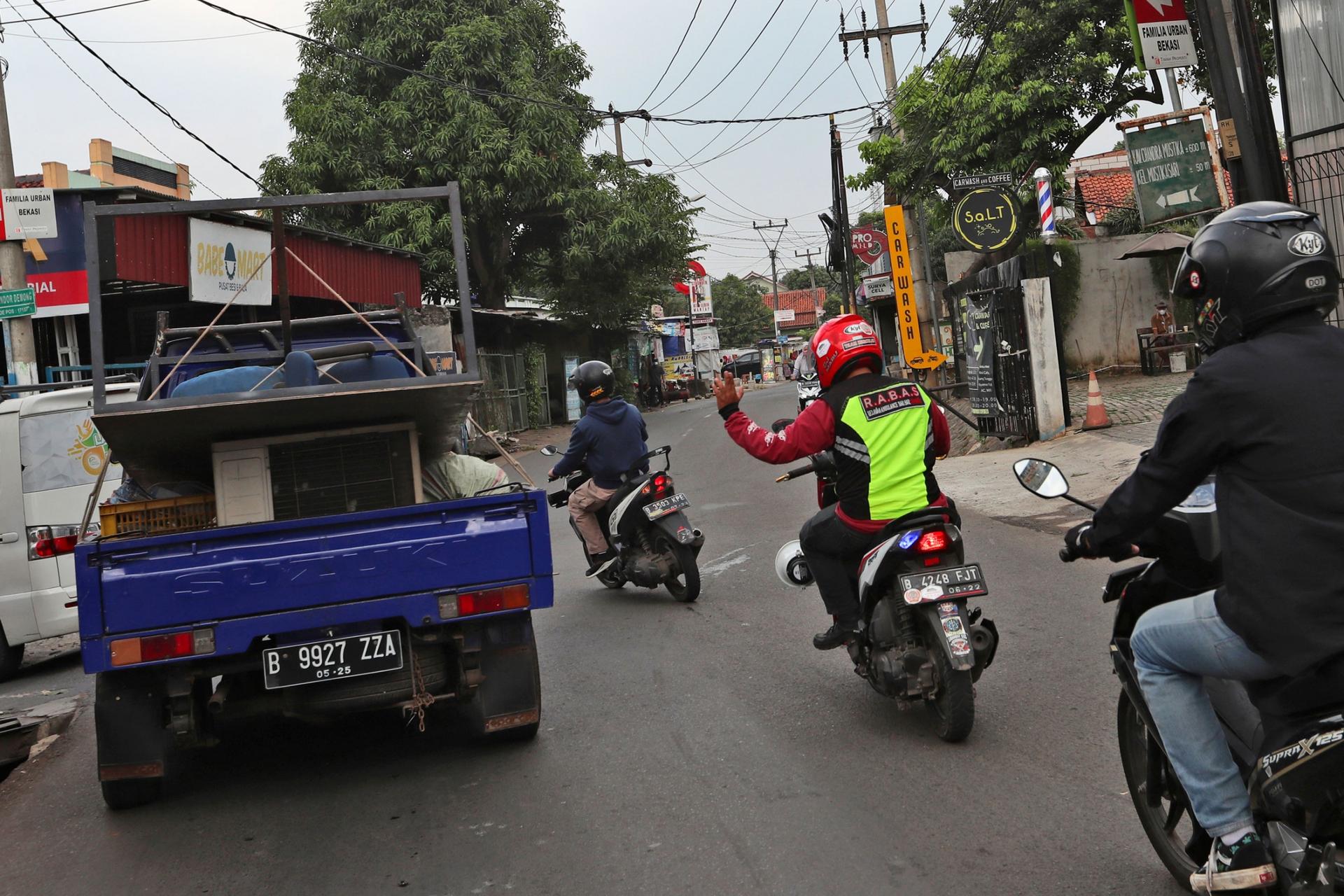 Three people on motorbikes are shown with one holding his hand up to a truck to clear the road for an ambulance.