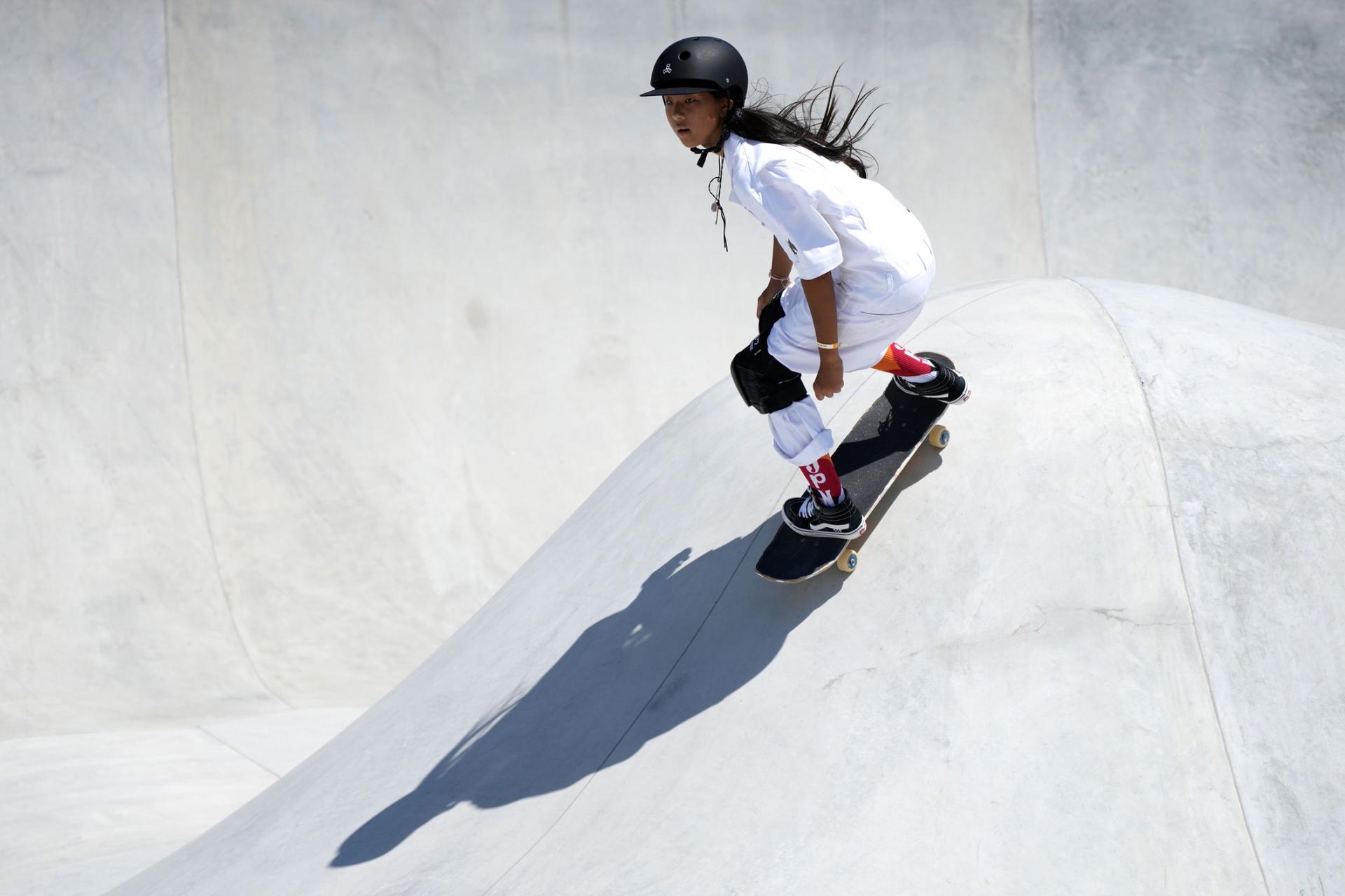 Kokona Hiraki is shown wearing all white and black knee pads while riding a skateboard.