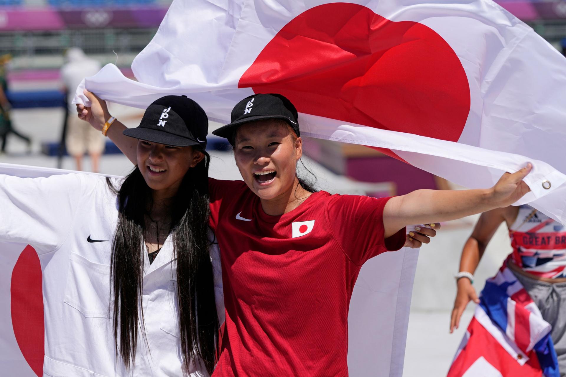 Sakura Yosozumi and Kokona Hiraki are show side-by-side with a Japanese flag held up behind them.