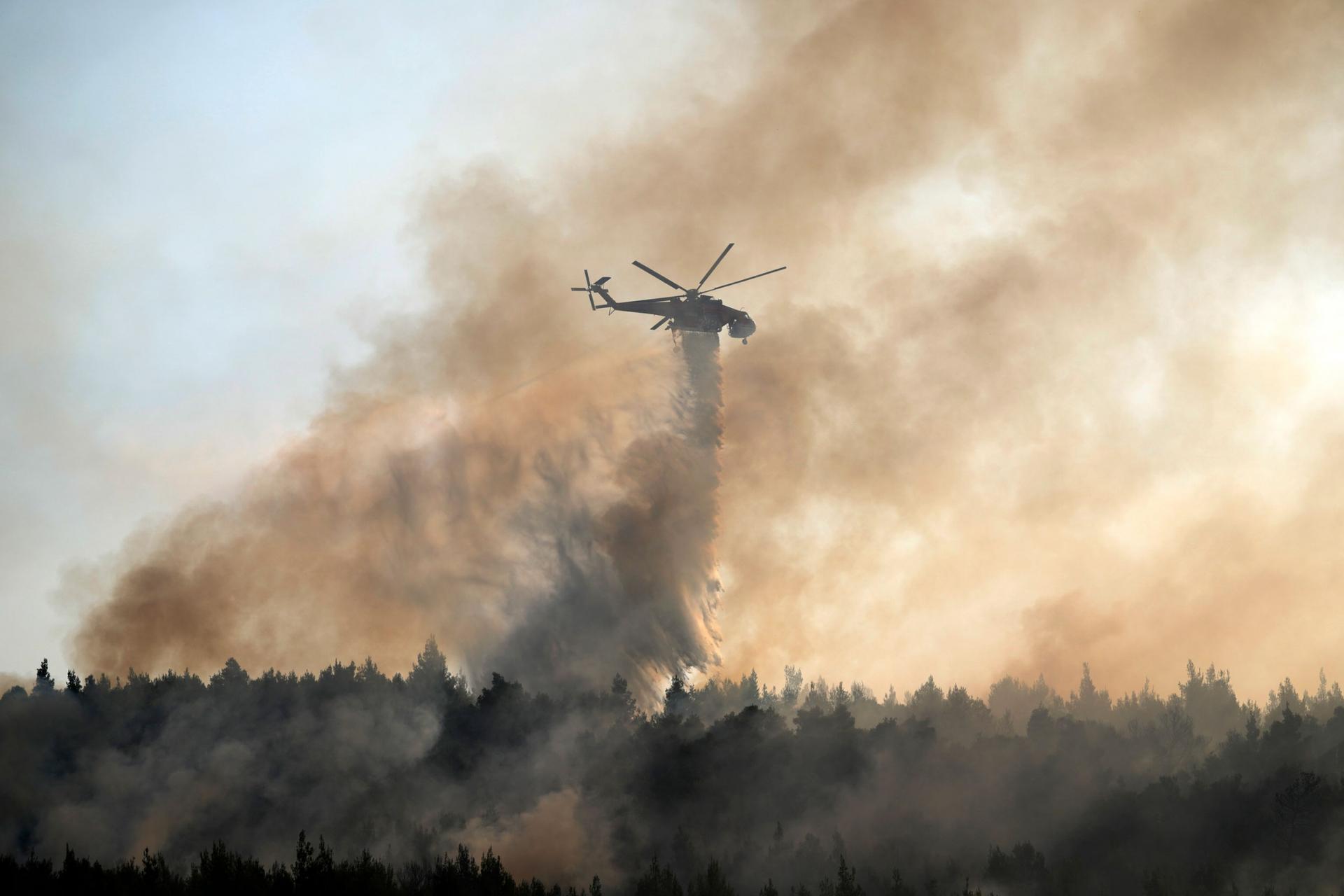 A helicopter is shown in the distance amid smoke rising up from the forest below.