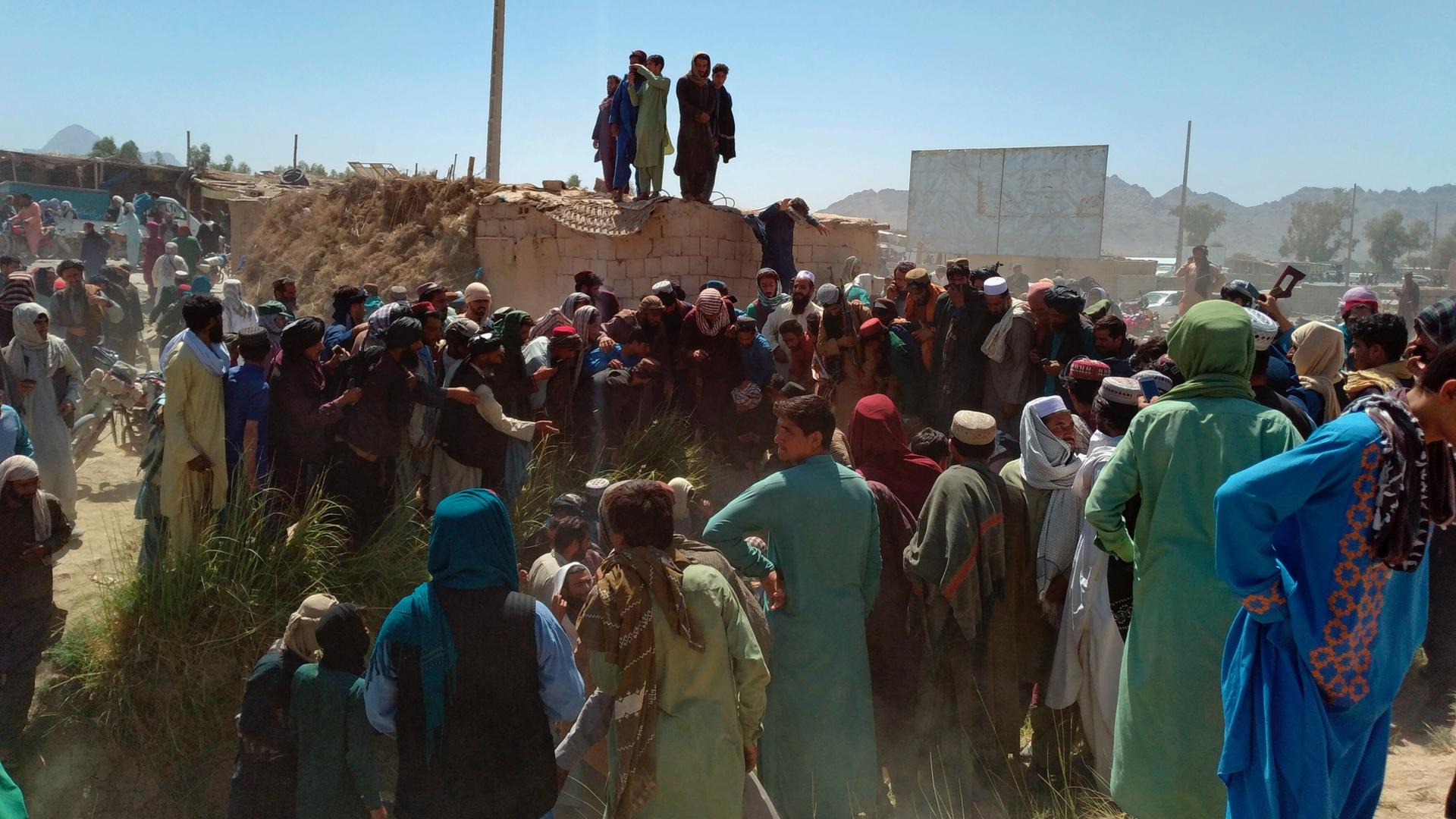 Taliban fighters and Afghans gather around the body of a member of the security forces who was killed