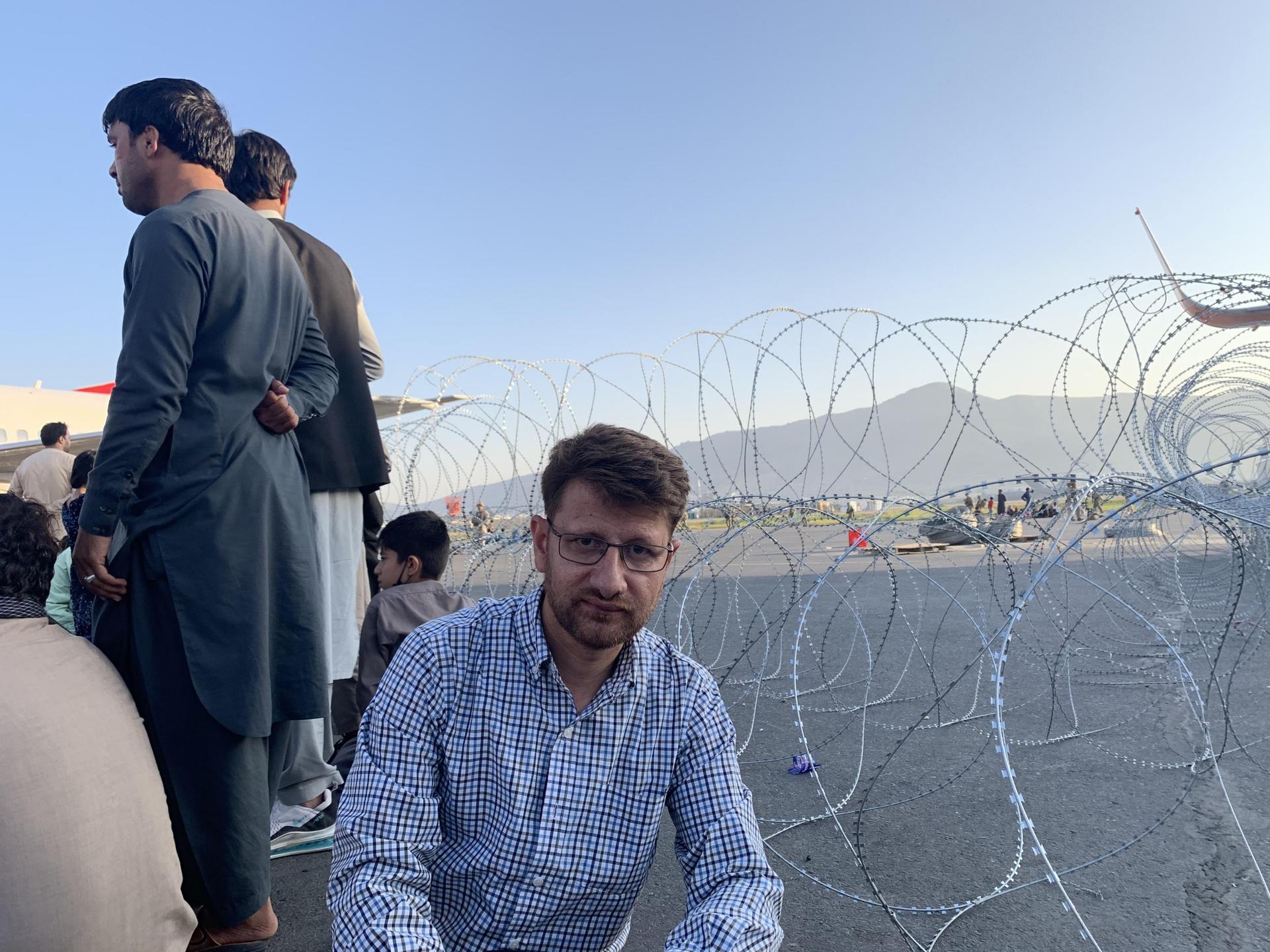 Hanif Sufizada kneeling besides a coil of barbed wire on the airport tarmac, amid a crowd of civilians