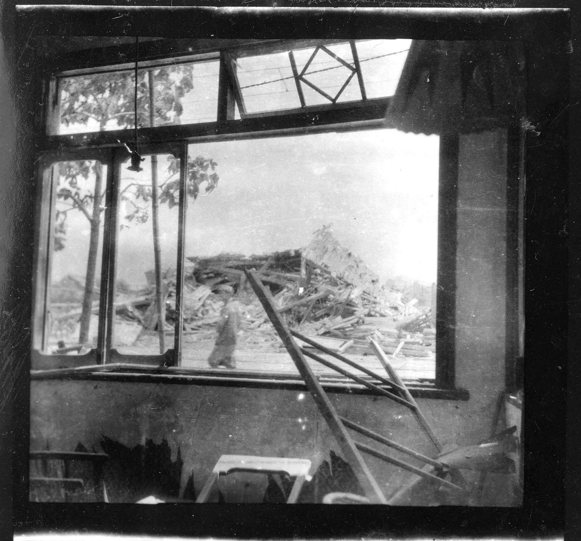 A pile of wooden rubble in the distance is shown through a blasted out window.