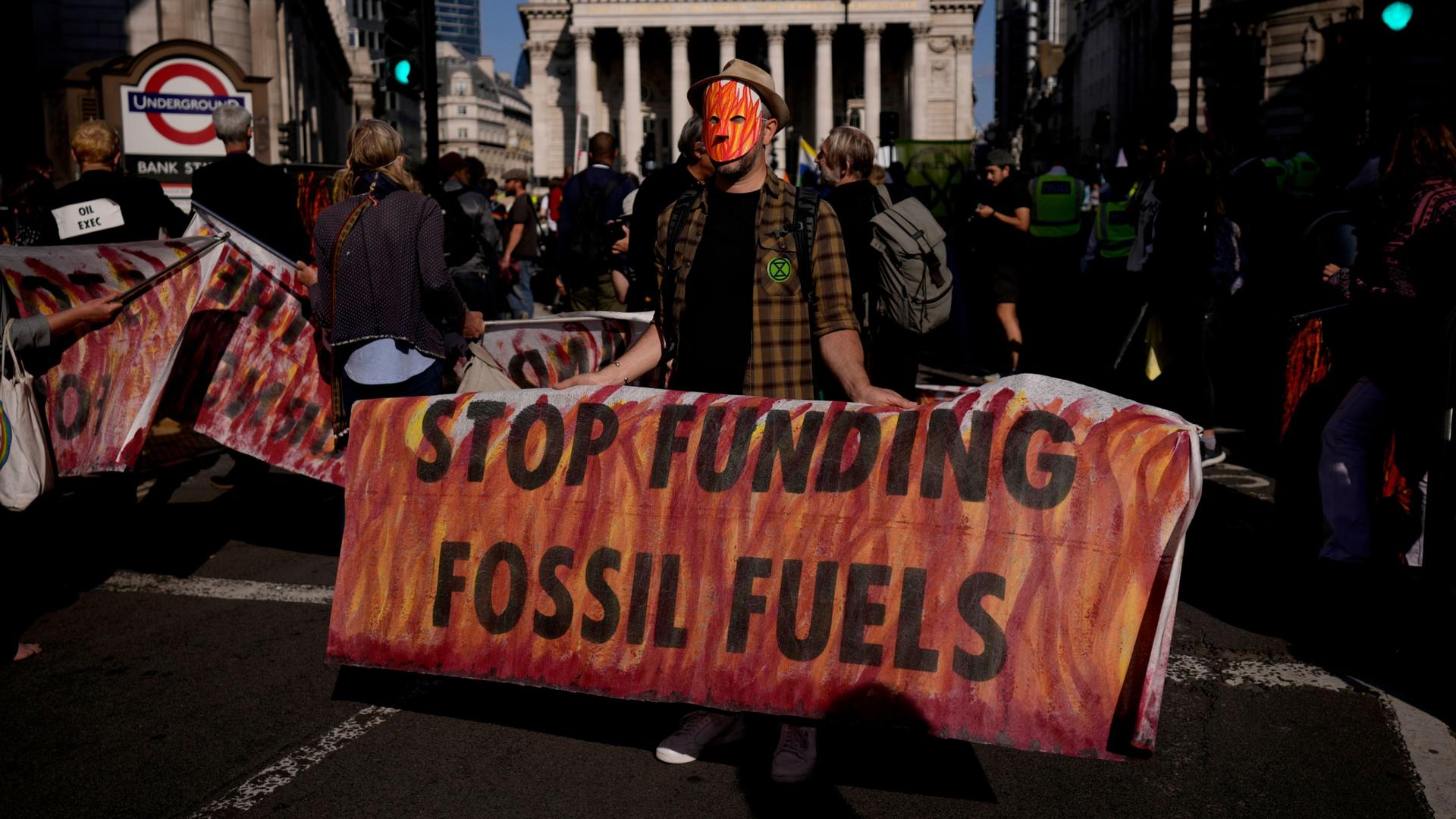 In this Thursday, Sept. 2, 2021 file photo, an Extinction Rebellion climate change activist holds a banner backdropped by the Bank of England, at left, and the Royal Exchange, center, in the City of London financial district in London. 