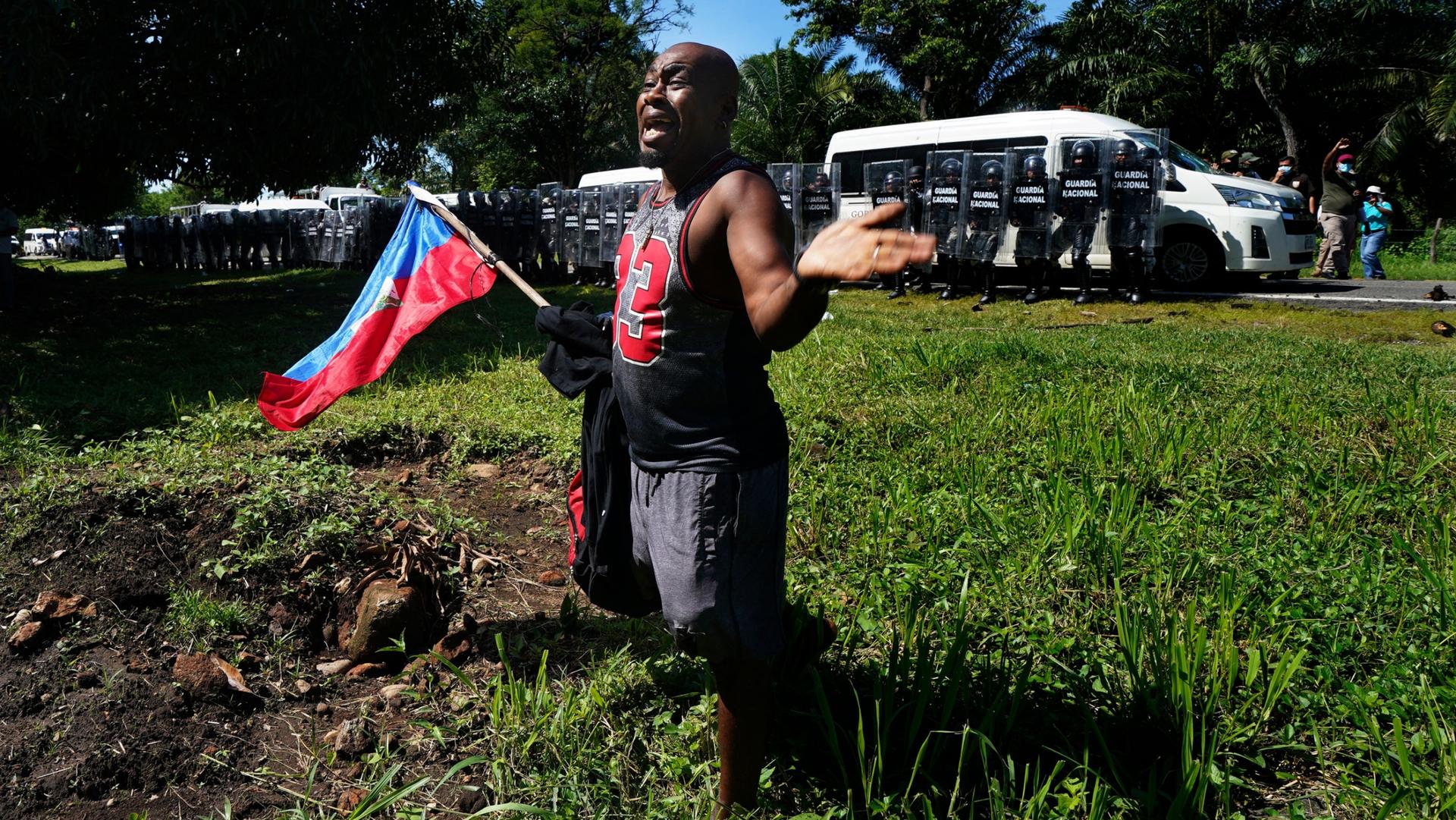 A Haitian migrant, holding his country's national flag, pleads with Mexican National guardsmen not to detain migrants making their way to the US-Mexico border, in Escuintla, Chiapas state, Mexico, Thursday, Sept. 2, 2021. 