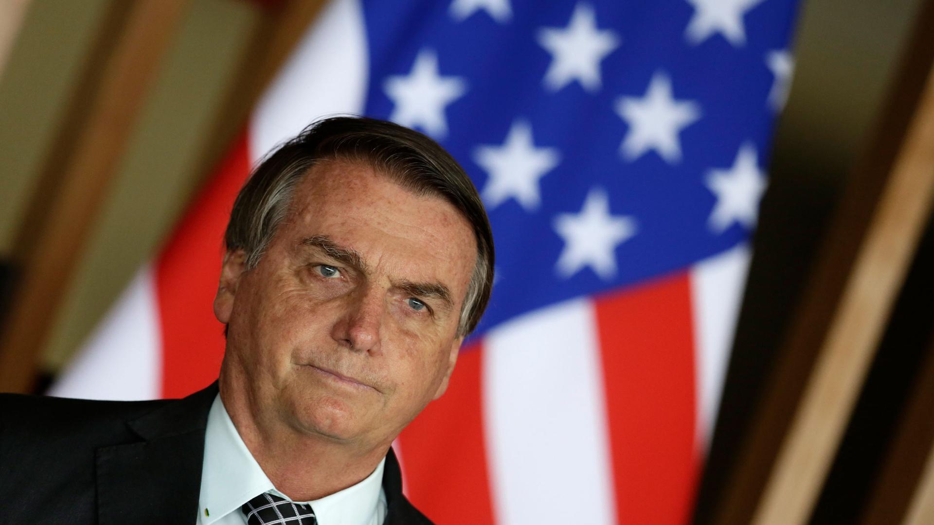 Brazil's President Jair Bolsonaro stands in front of a US flag during a news conference at Itamaraty Palace in Brasilia, Brazil, Tuesday, Oct. 20, 2020. 