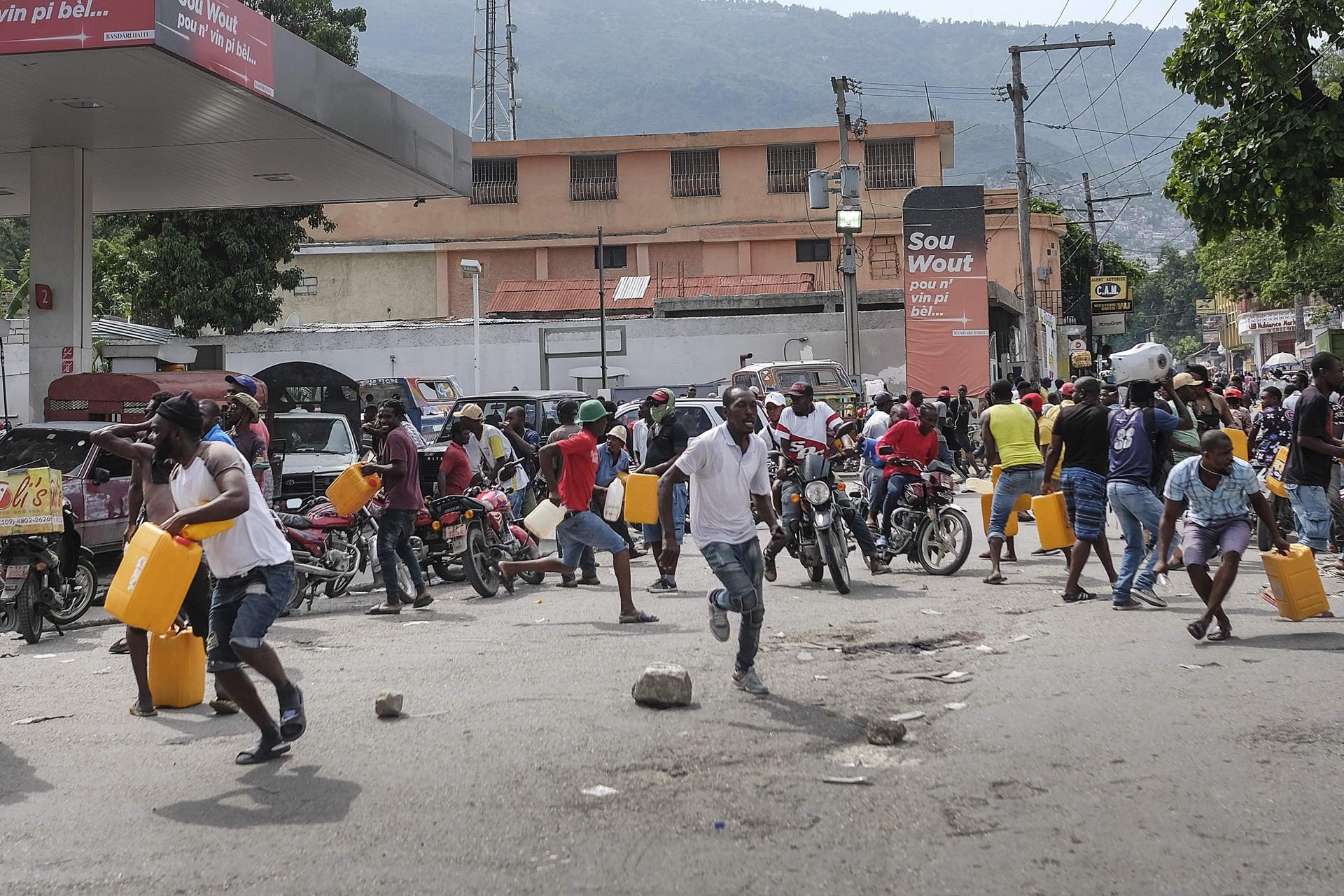 People run for cover as police shoot into the air to disperse a crowd threatening to burn down a gas station because they believed the station was withholding the gas, in Port-au-Prince, Haiti, on Oct. 23, 2021. The ongoing fuel shortage has worsened, wit