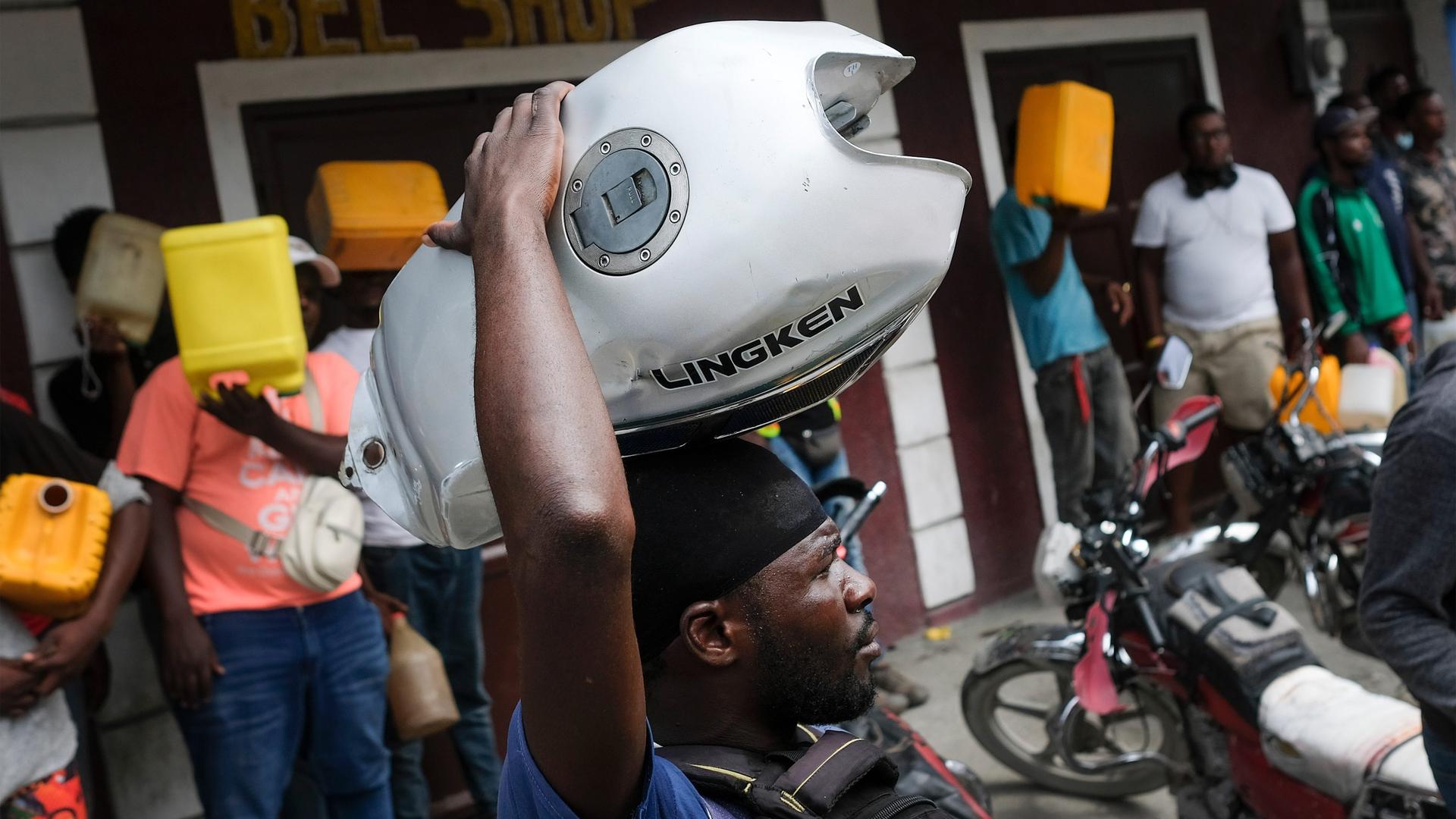 A man balances his motorbike tank on his head as he waits outside a gas station in hopes of filling his tank, in Port-au-Prince, Haiti, on Oct. 23, 2021. The ongoing fuel shortage has worsened, with demonstrators blocking roads and burning tires in Haiti'