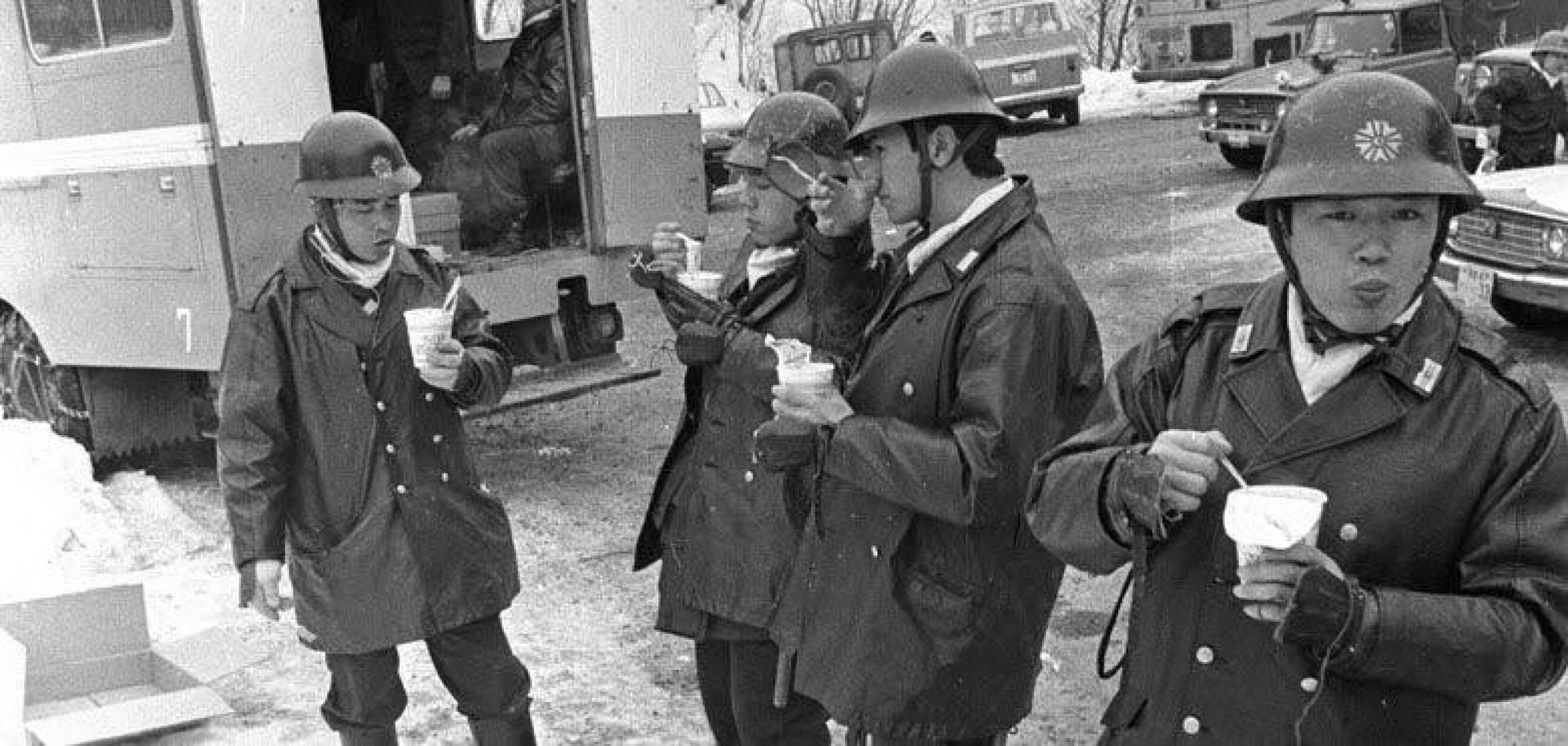 Black and white photo of Japanese policemen in coats and helmets eating Cup Noodles
