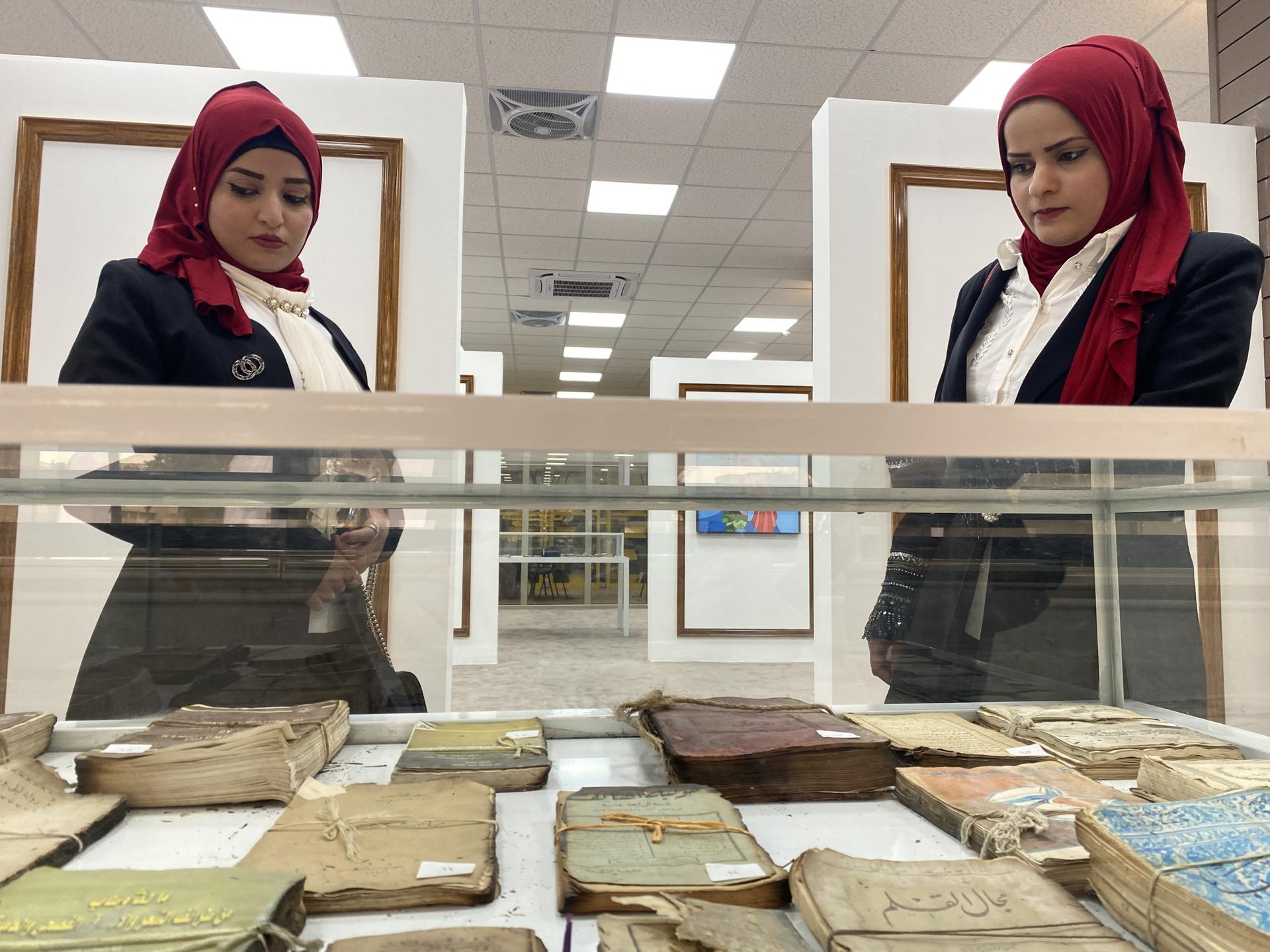 Ghufran Abdelmalek (right) and her sister Rahma Abdelmalek (left) peer at books salvaged from the ruins of the destroyed University of Mosul Central Library on Feb. 19, 2022. 
