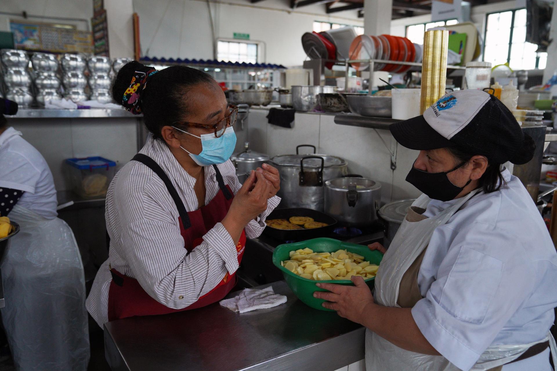 Luz Dary Cogollo (left) and one of her workers prepare ajiaco soup at the Perseverancia market in Bogotá. The soup is based on potatoes, whose price has risen steeply over the past year. 