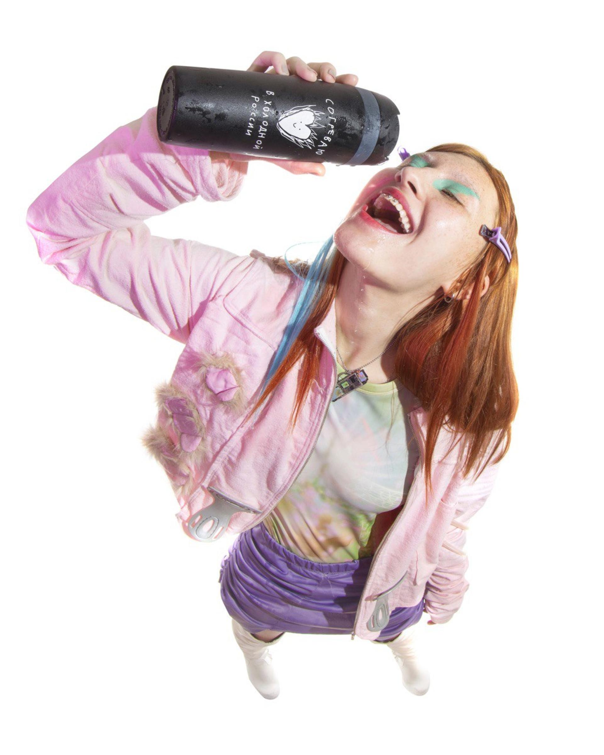 a woman in pink shown in a distorted perspective drinking out of a thermos