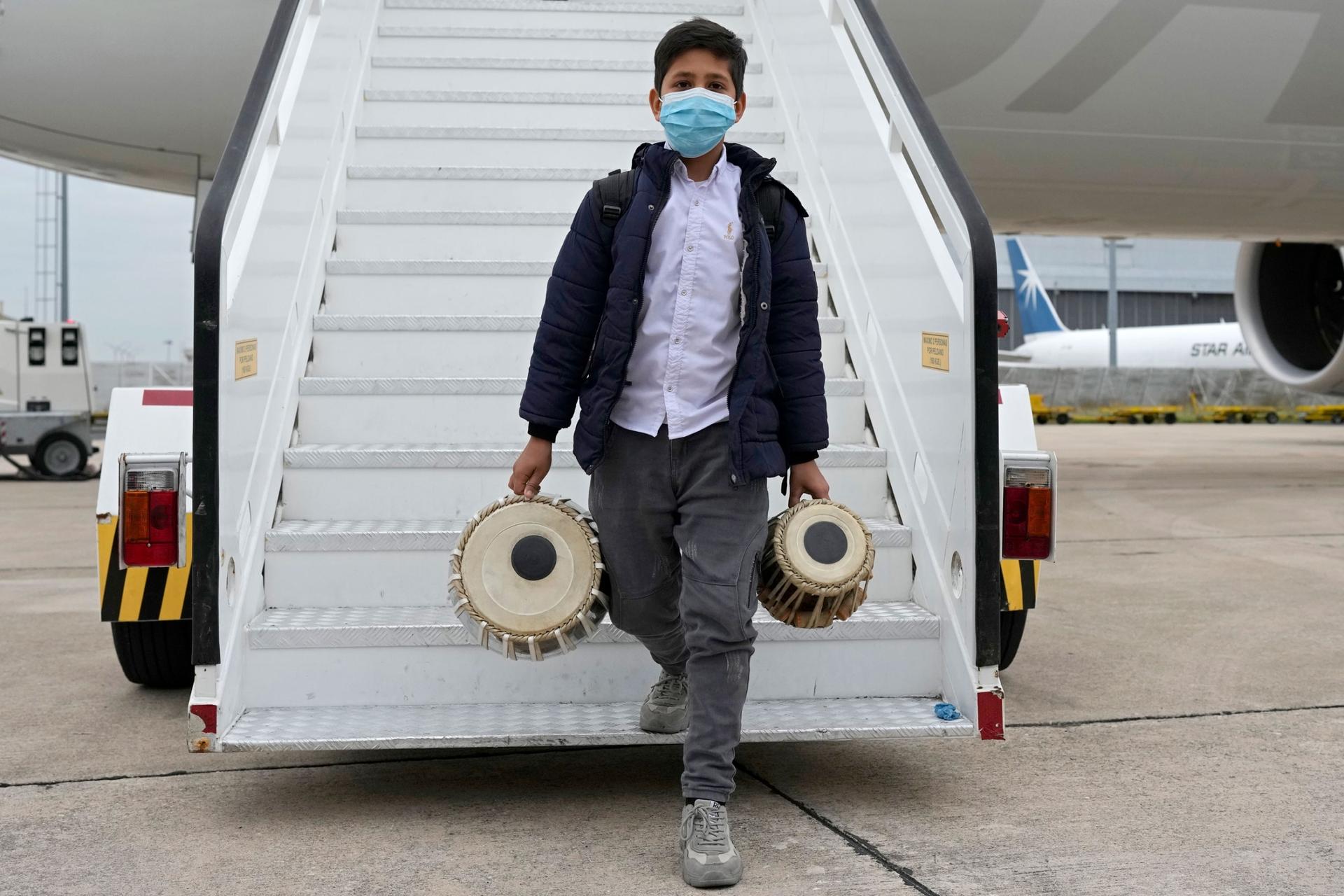 An Afghan boy carrying musical instruments disembarks from an airplane at Lisbon military airport, Monday, Dec. 13, 2021. 