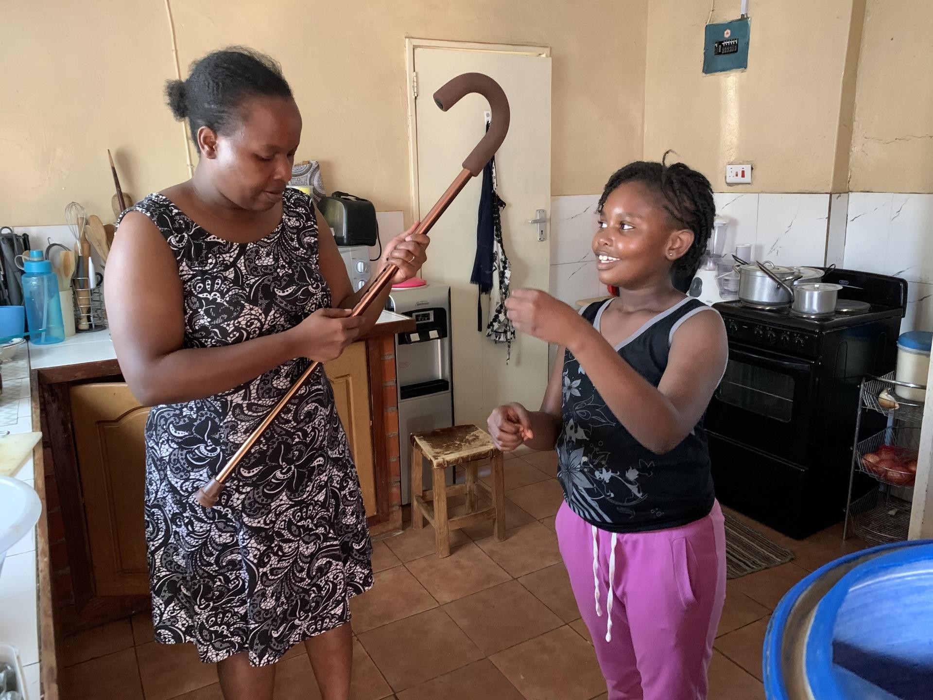 Nala Phiri adjusts the length of her cane while in the kitchen with her daughter Namila. Her leg weakness had progressed to the point where she had to walk using a cane. It has improved since being on treatment for multiple sclerosis.