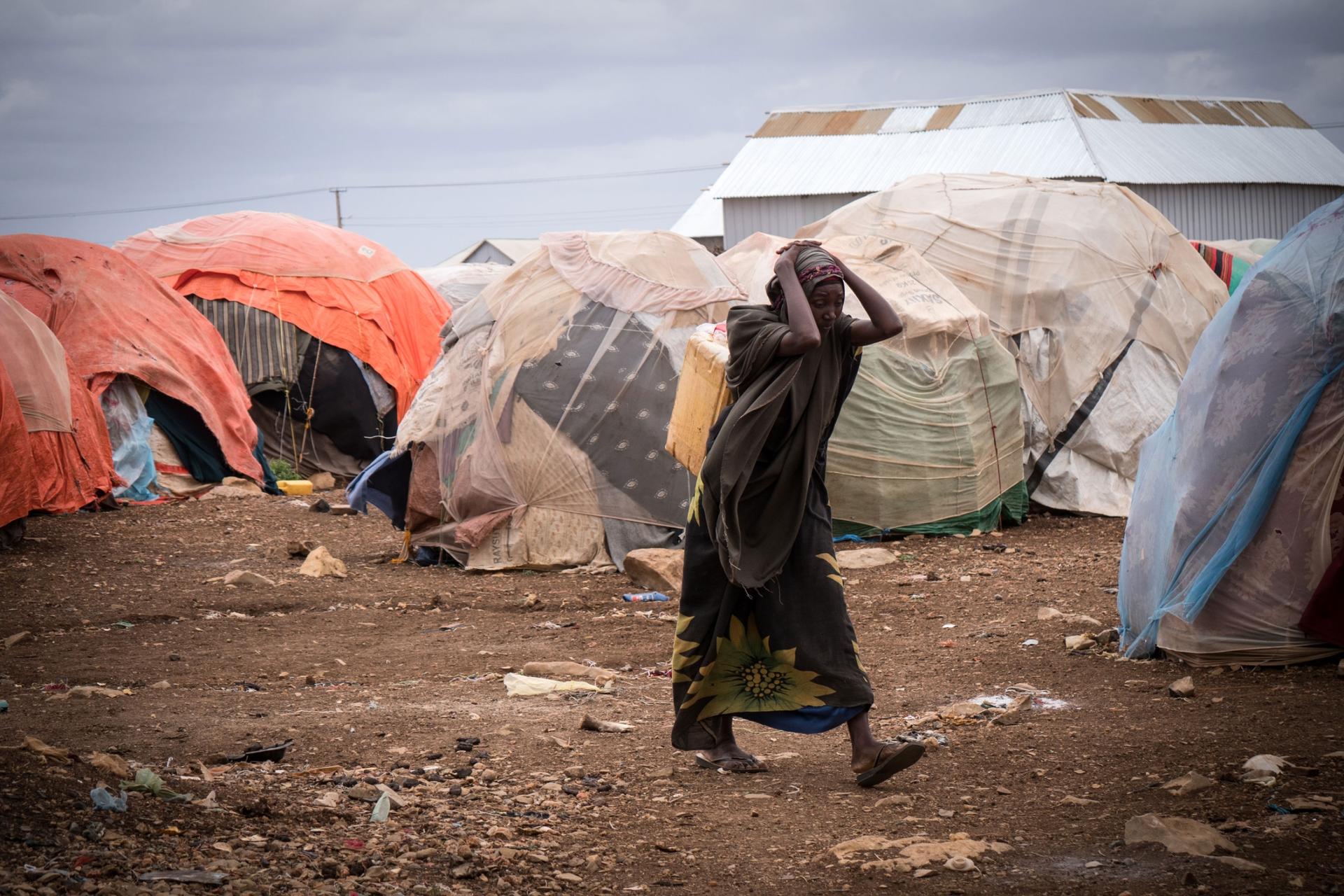 A displaced woman in front of orange- and white-covered tents at a camp in Baidoa, Somalia. 