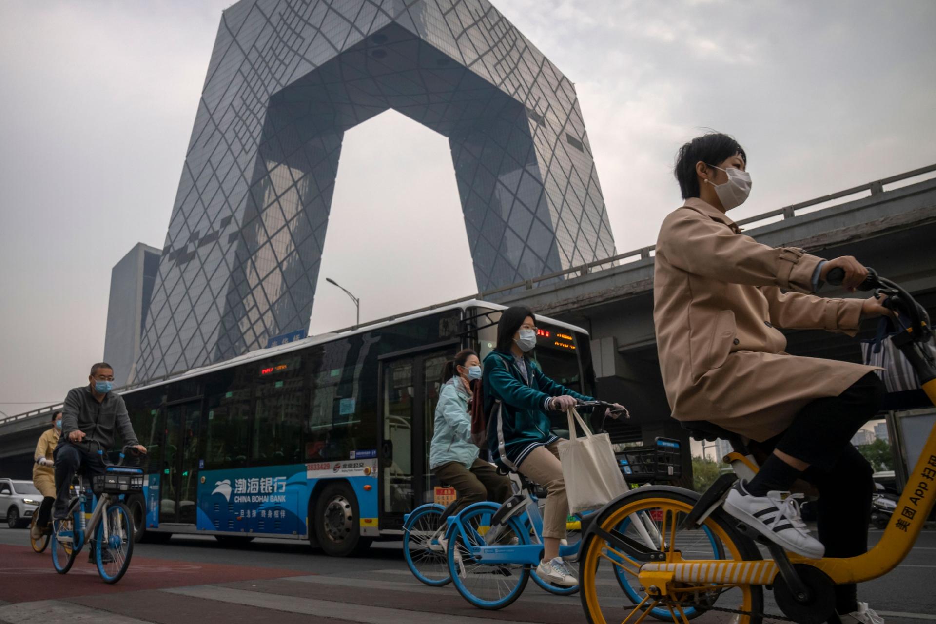 Commuters wearing face masks ride bicycles along a street in the central business district in Beijing, Thursday, Oct. 20, 2022.