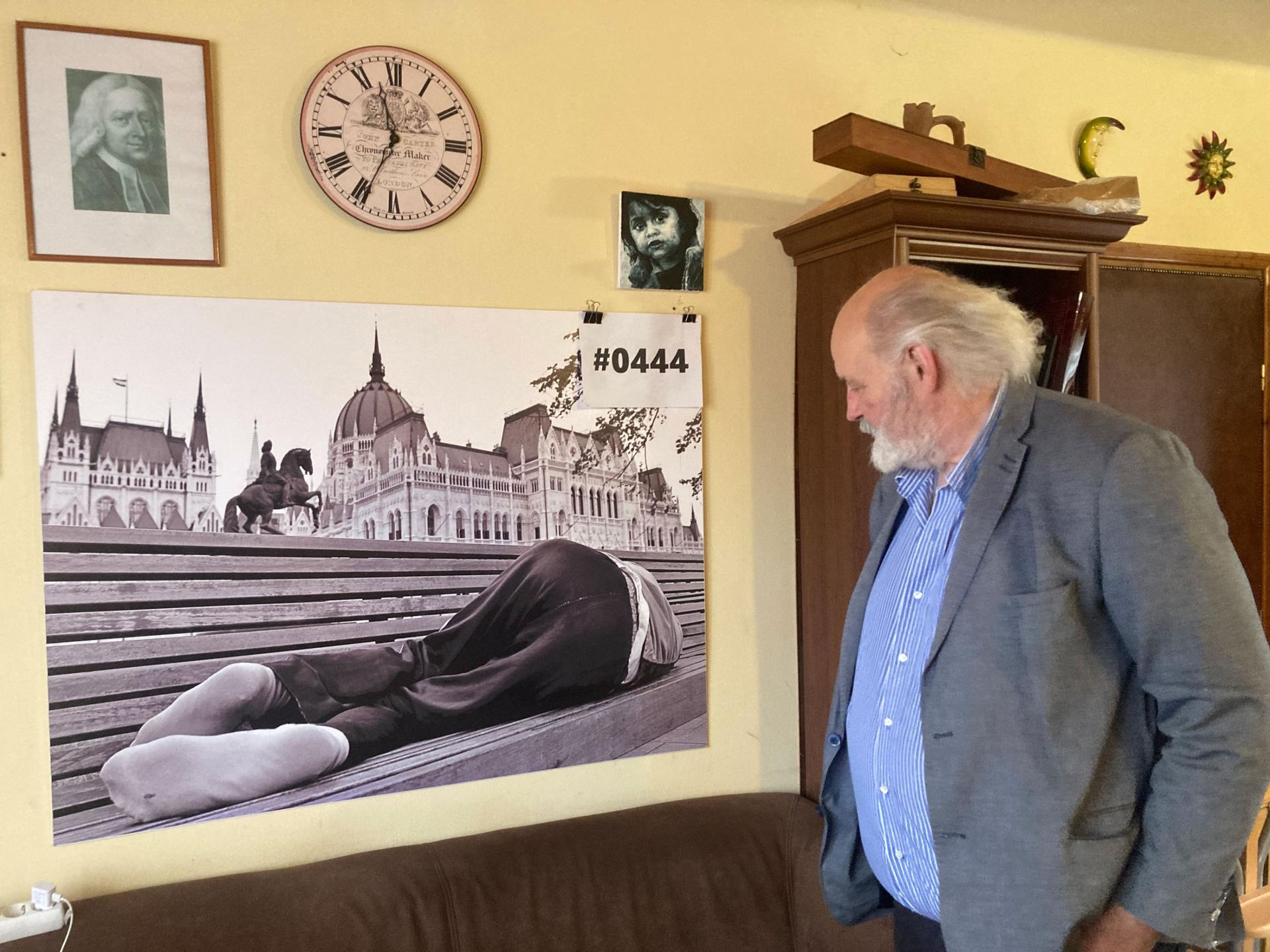 Pastor Iványi in front of a photo of an unhoused person sleeping in front of the Parliament building that hangs in his church office. 
