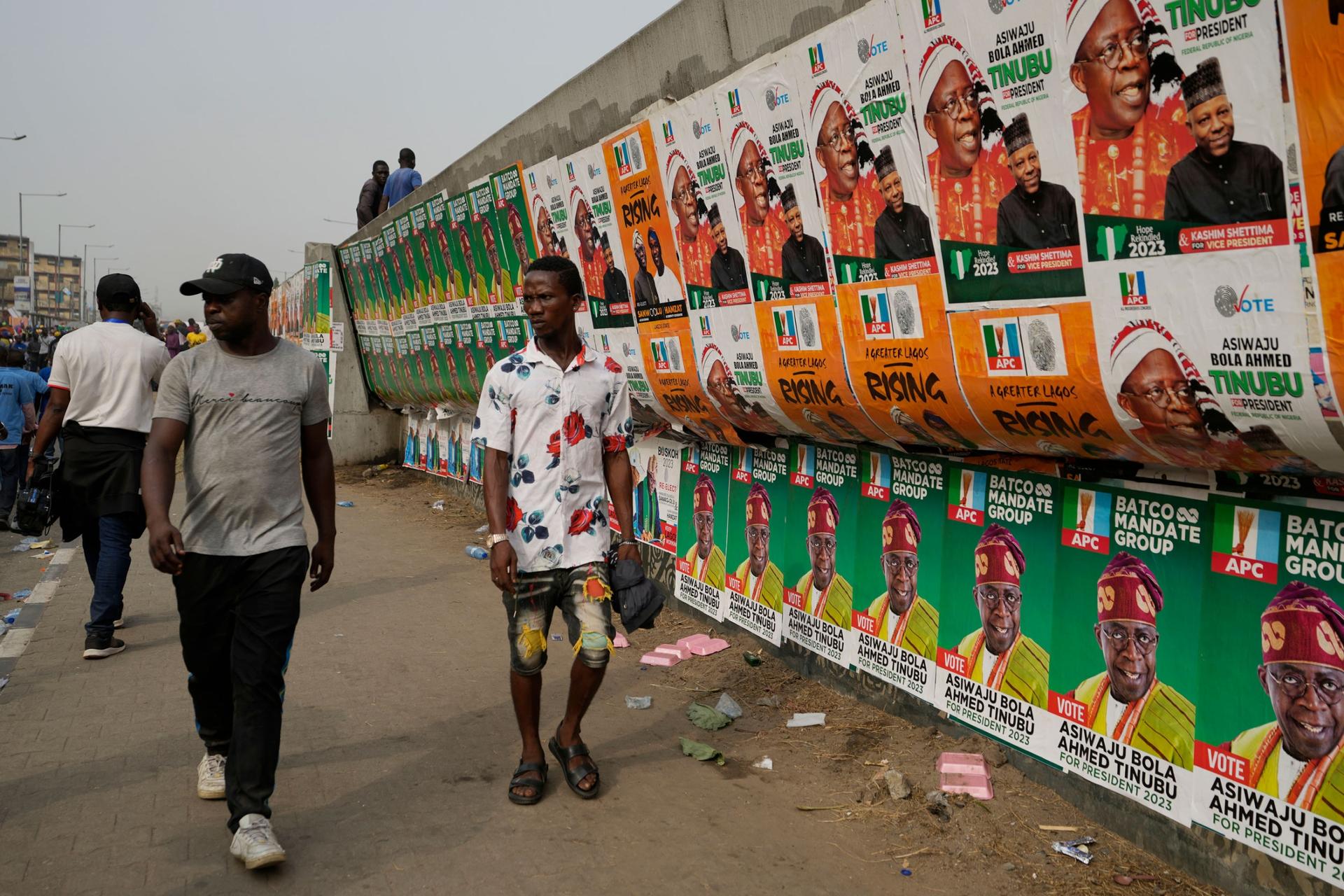 People walk past election campaign posters of Bola Ahmed Tinubu, presidential candidate of the All Progressives Congress, Nigeria ruling party during an election campaign rally at the Teslim Balogun Stadium in Lagos Nigeria, Tuesday, Feb. 21, 2023. 