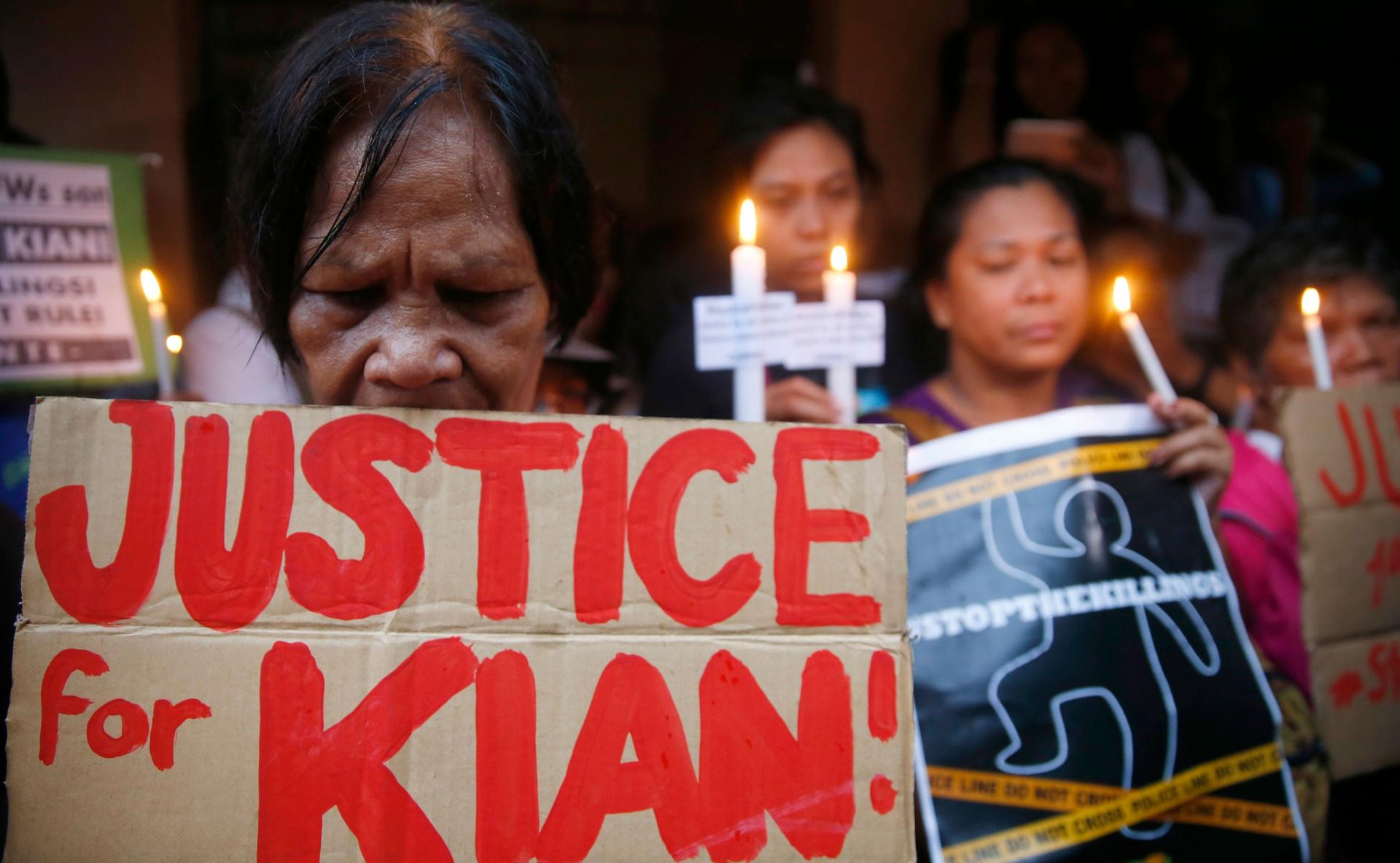 In this Aug. 21, 2017, file photo, protesters display placards and light candles outside the wake for slain Kian Loyd Delos Santos.