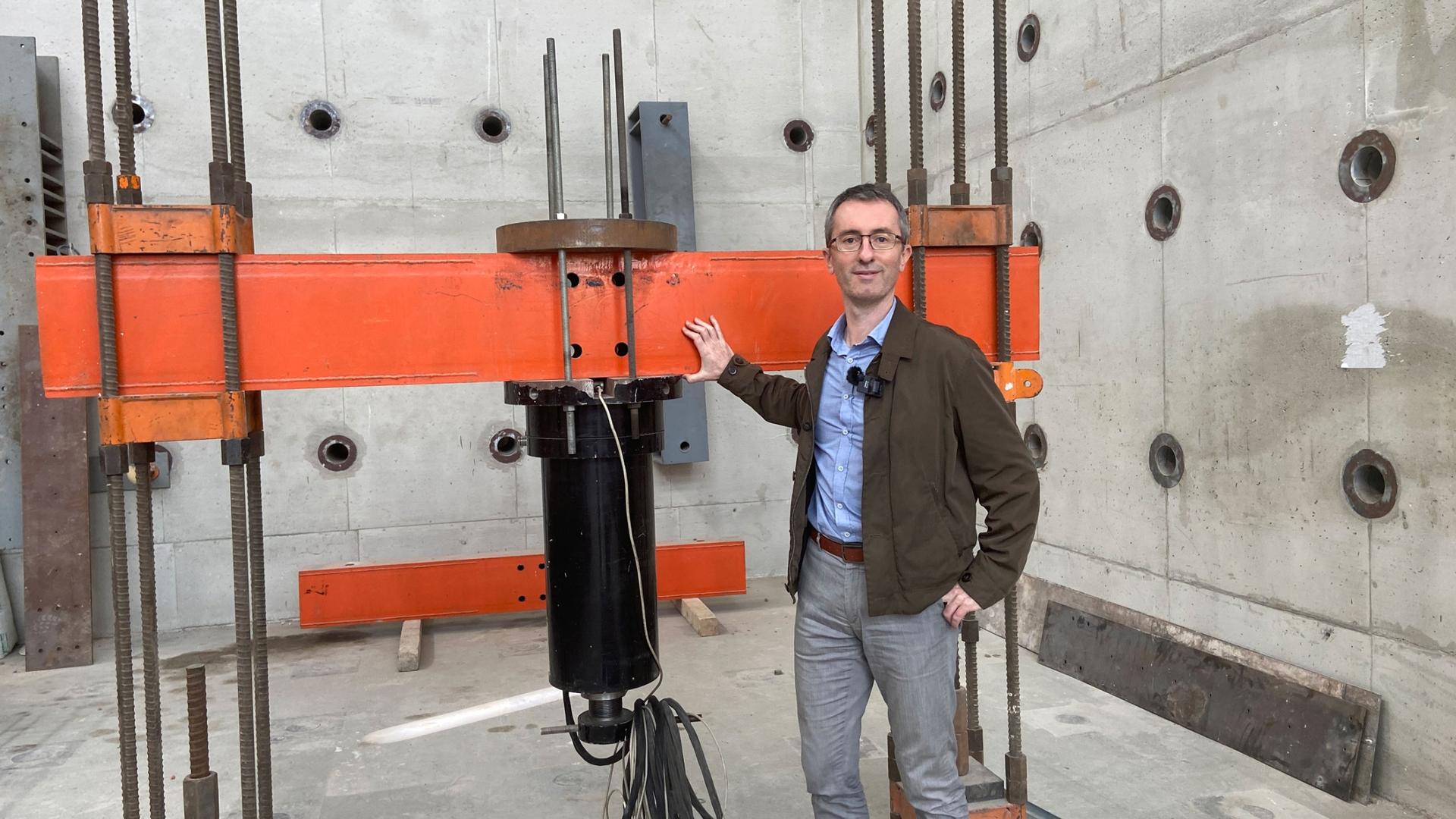 Dr. José M. Adam, chief researcher at the Institute of Science and Concrete Technology, stands next to a hydraulic jack capable of applying tons of load pressure on simulated bridges and buildings. 