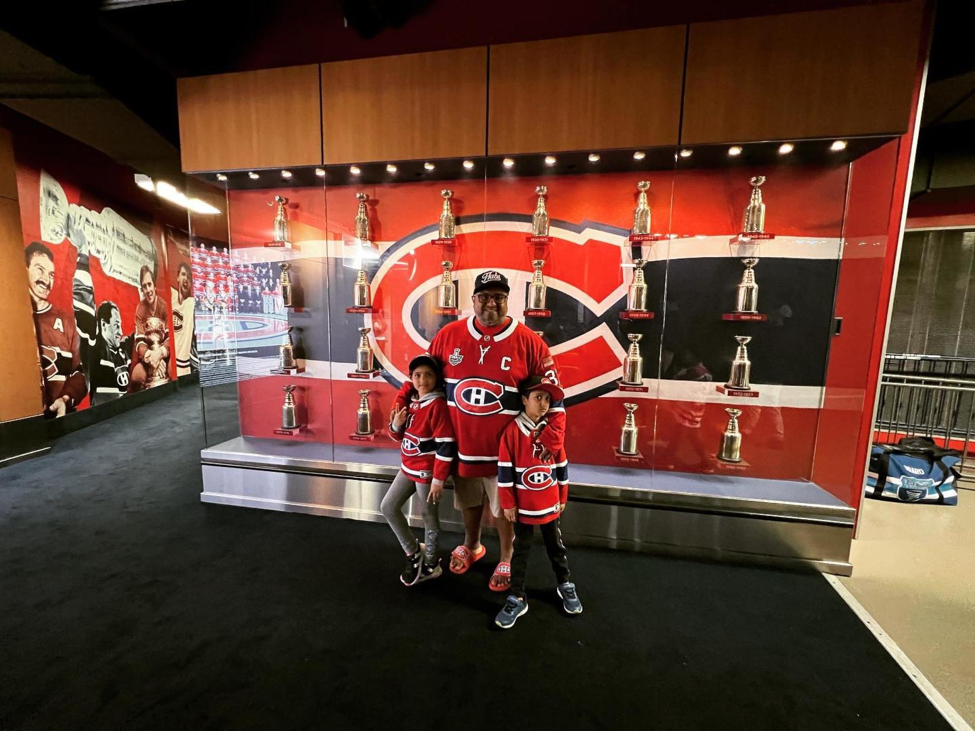 Montreal Canadiens superfan, Sunil Peetush, standing with his son and daughter in team jerseys in front of a trophy case