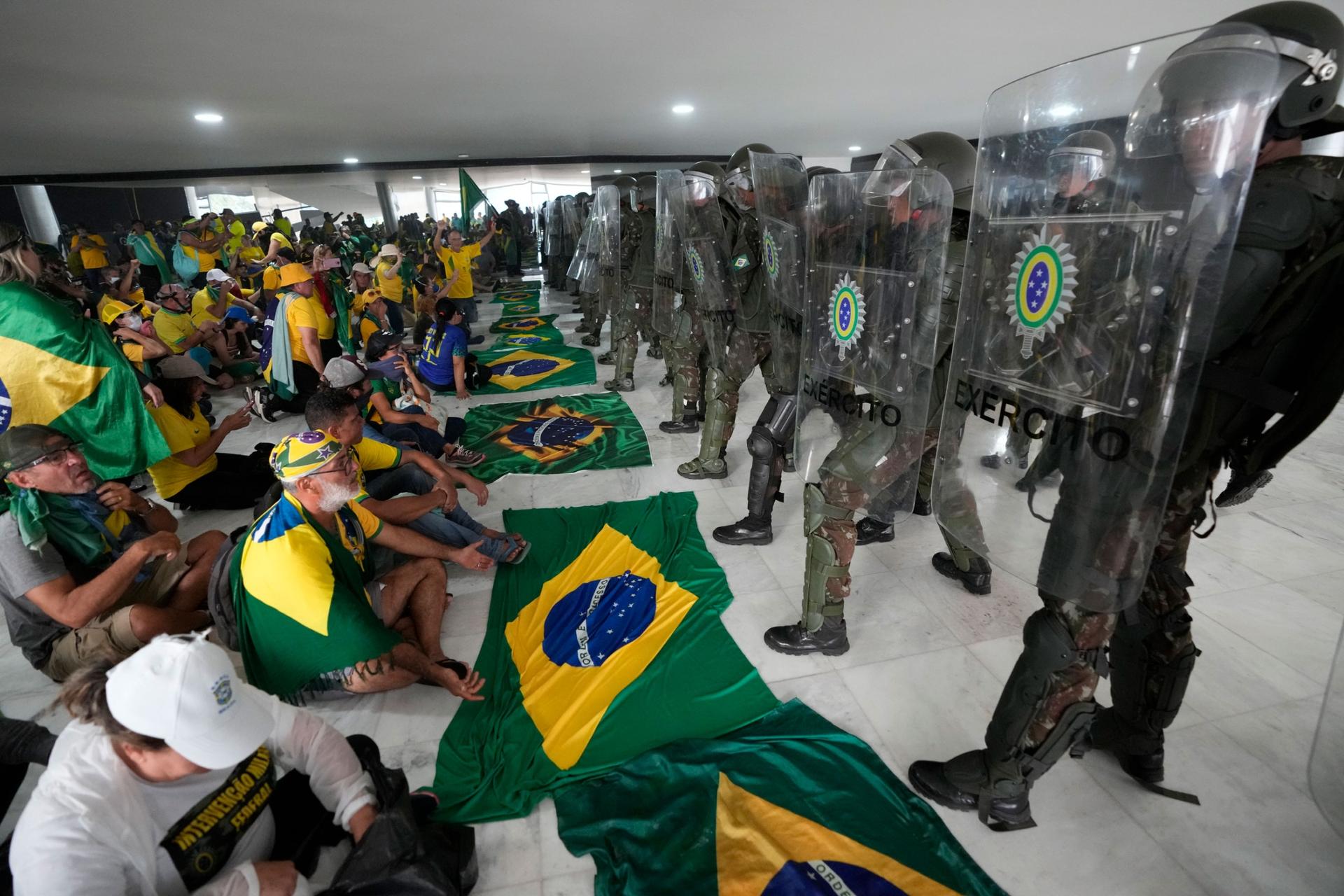 Supporters of Brazil's former President Jair Bolsonaro, sit in front of police inside the Planalto Palace after storming it, in Brasilia, Brazil, Jan. 8, 2023. 