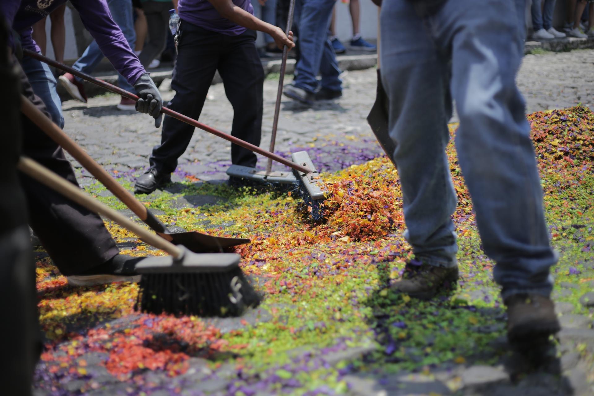 A cleaning crew picks up the remains of an alfombra following a Holy Week procession.