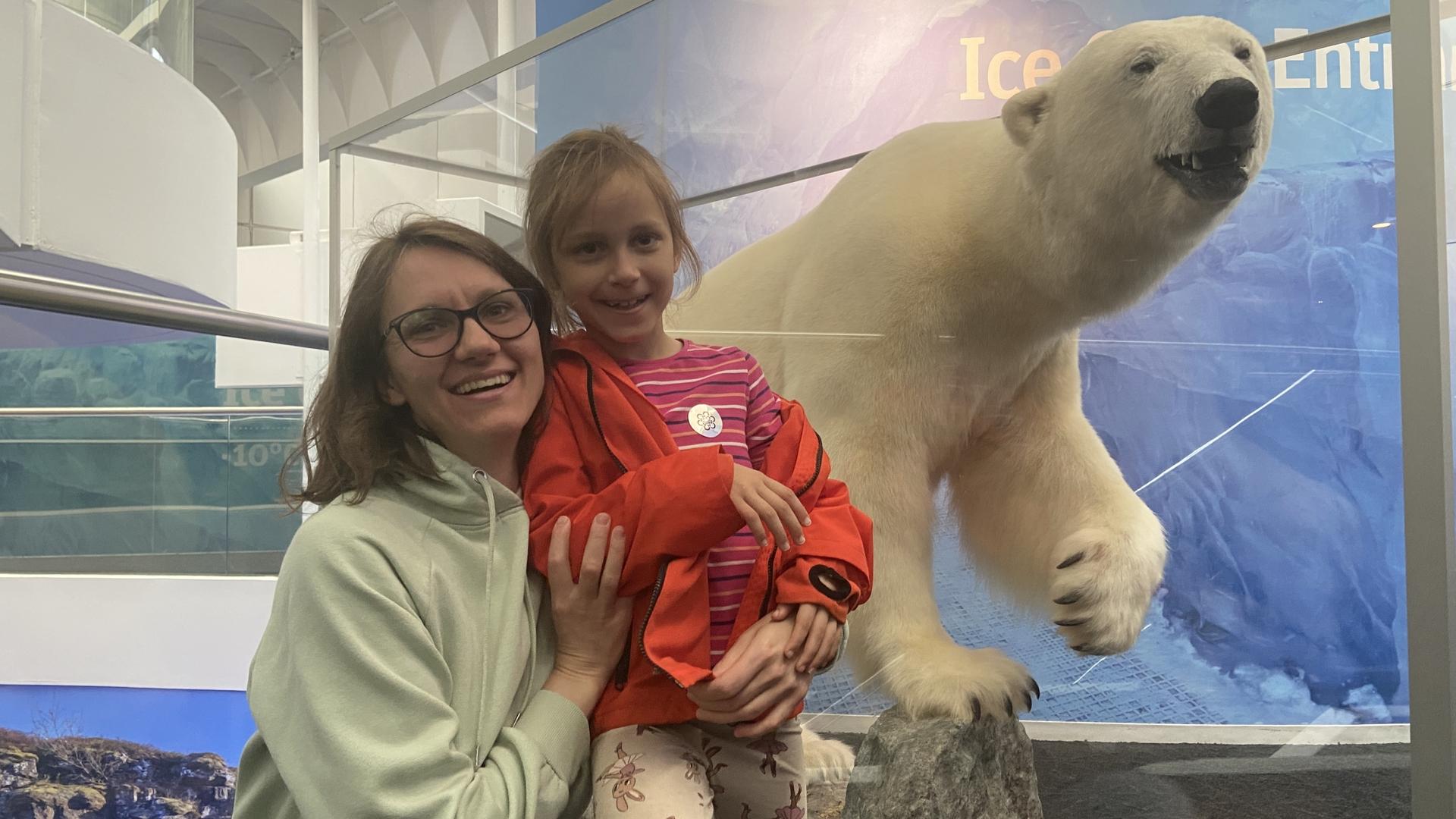 a mother holding her daughter in front of a sculpture of a polar bear